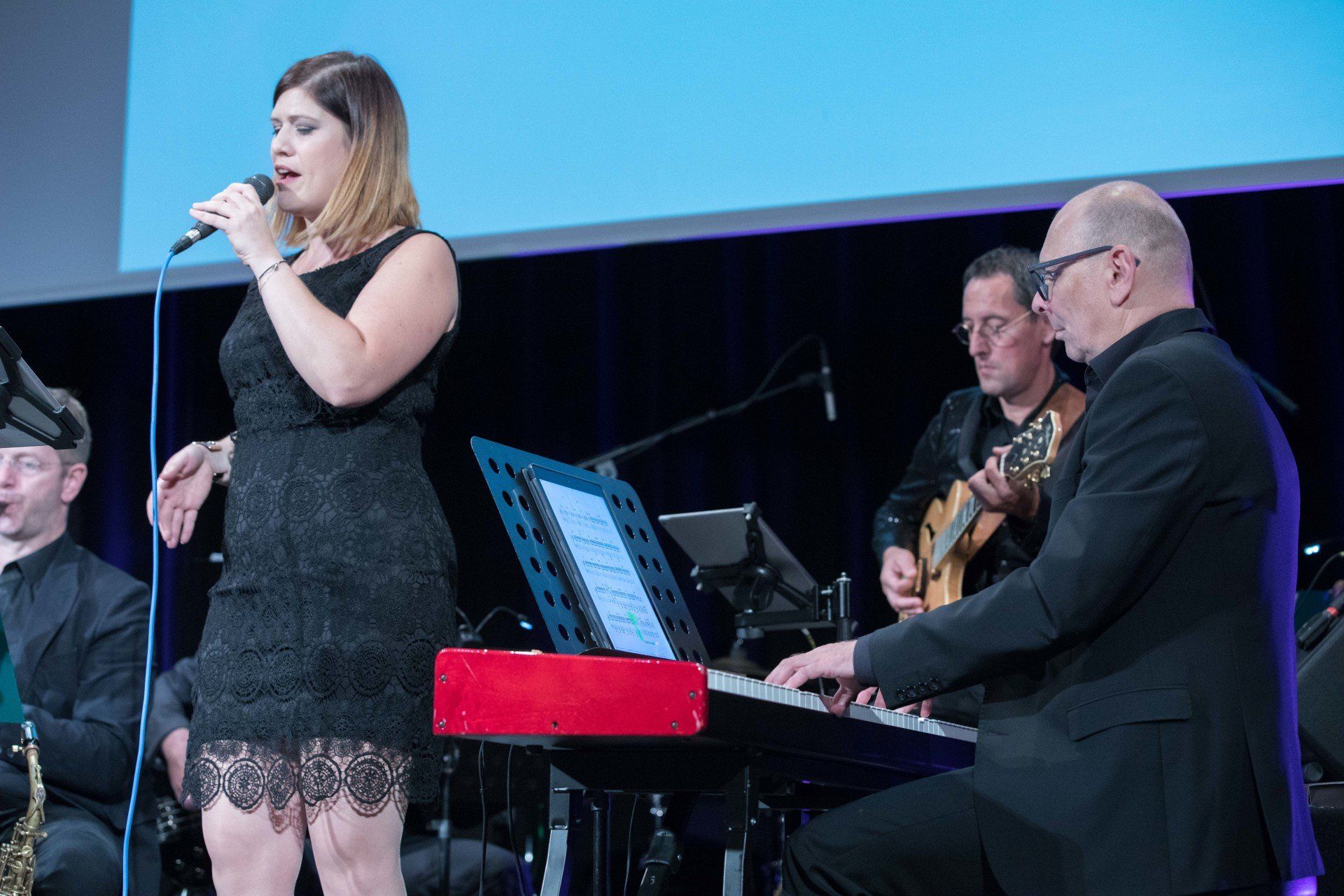 Eine Frau singt in ein Mikrofon, während ein Mann Klavier spielt.