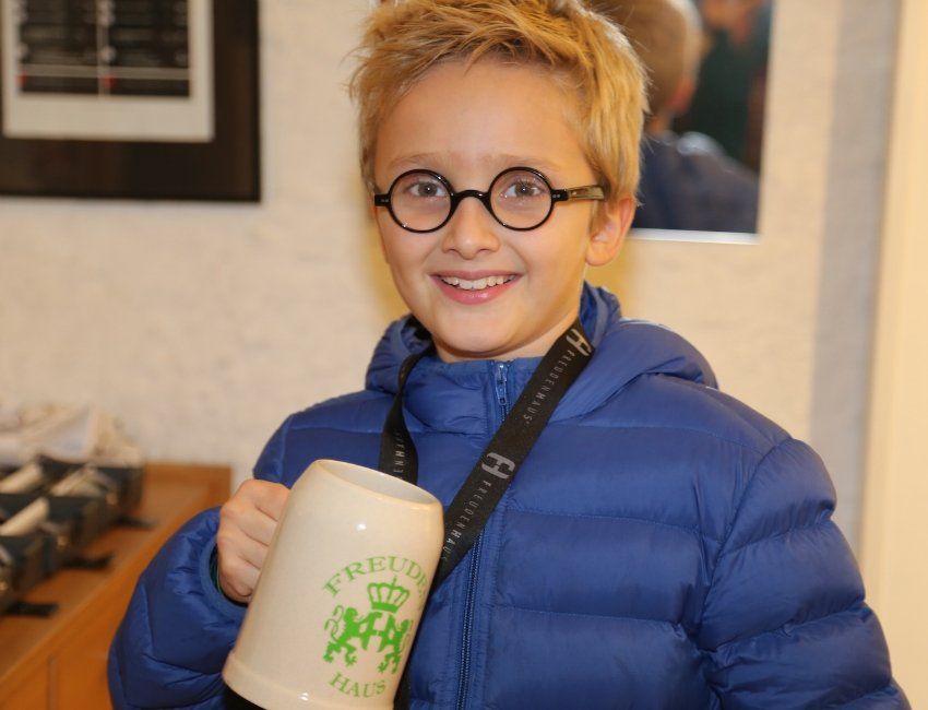 Ein kleiner Junge mit Brille und blauer Jacke hält eine Tasse mit der Aufschrift „Prinzessin“
