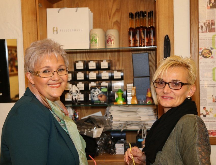 Zwei Frauen stehen nebeneinander vor einem Regal mit Flaschen darauf