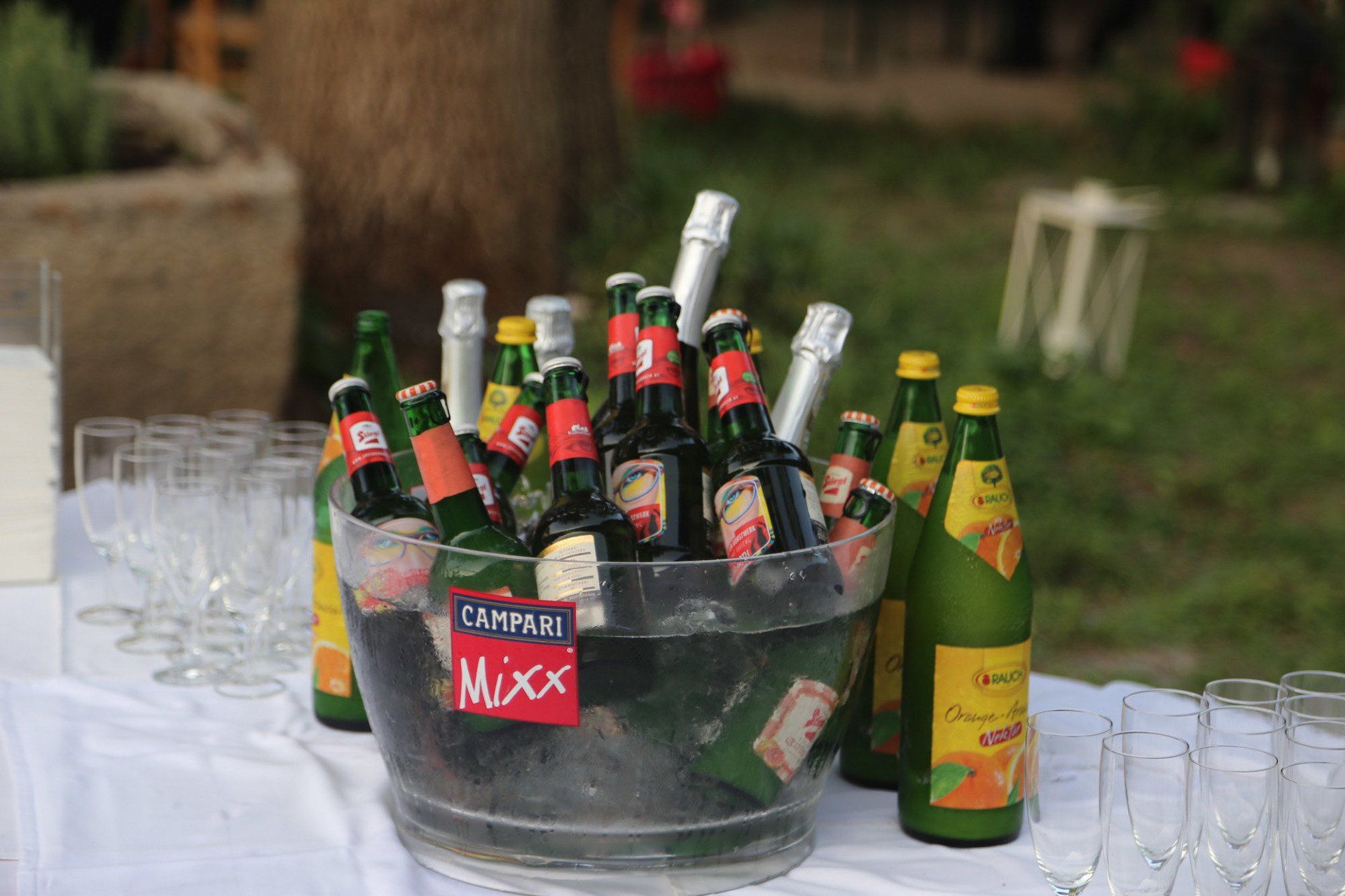 Auf einem Tisch mit Gläsern steht ein Eimer voller Campari-Flaschen.
