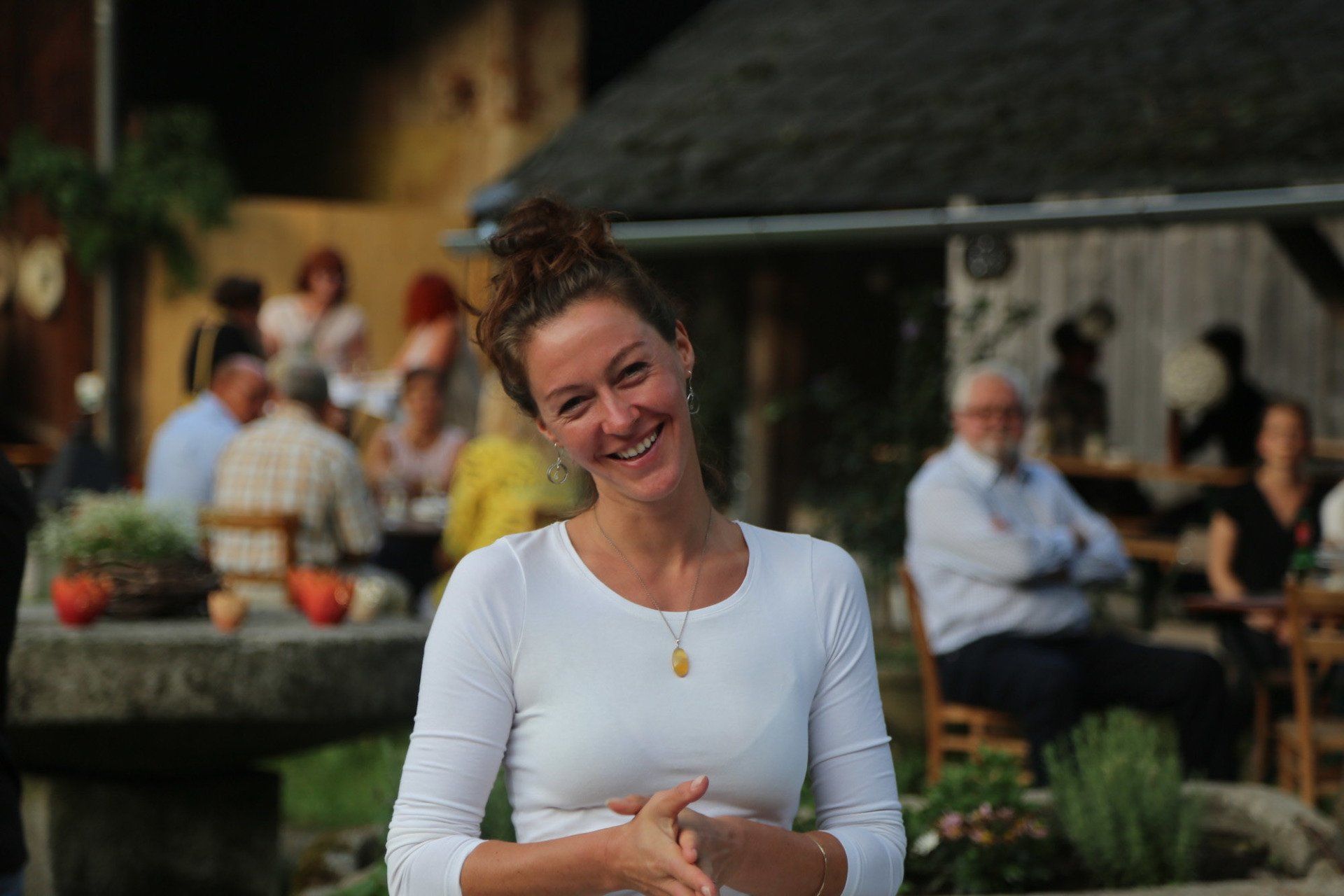 Eine Frau in einem weißen Hemd lächelt vor einer Gruppe von Menschen.