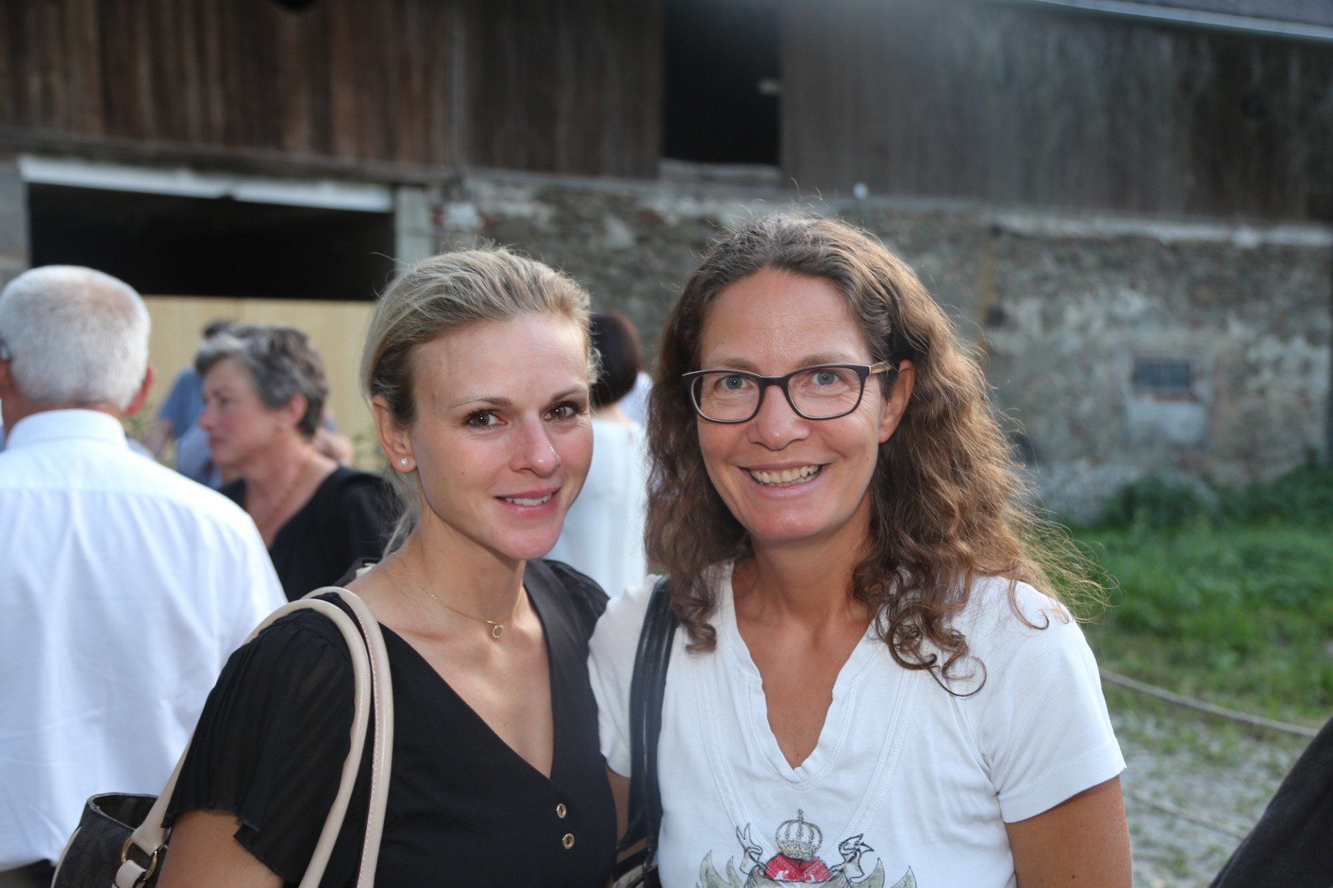 Zwei Frauen stehen nebeneinander und lächeln in die Kamera.