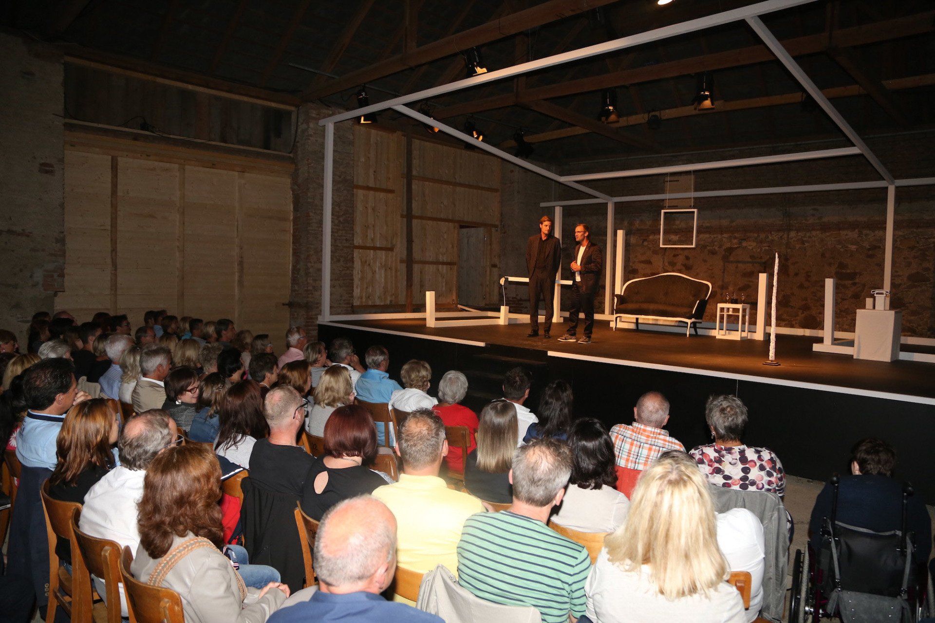 Eine große Gruppe von Menschen sitzt vor einer Bühne und sieht sich ein Theaterstück an.