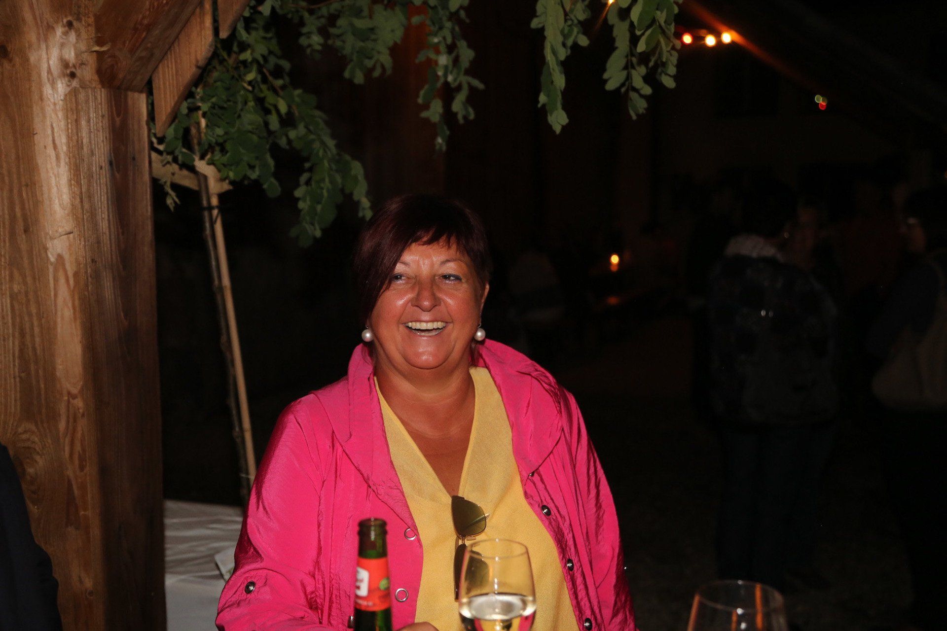 Eine Frau in einer rosa Jacke hält ein Glas Wein.