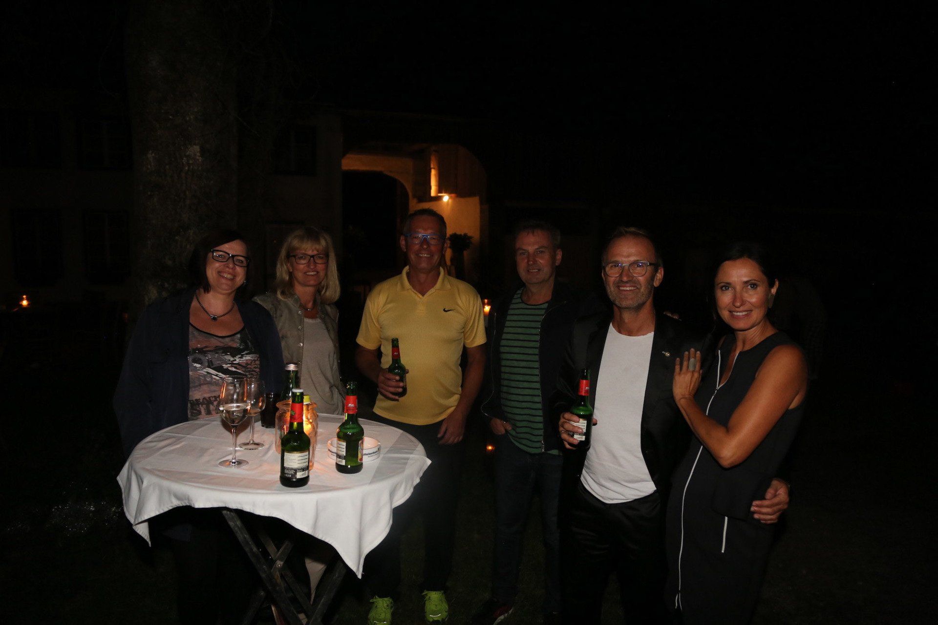 Eine Gruppe von Menschen steht um einen Tisch herum, auf dem Weinflaschen stehen.