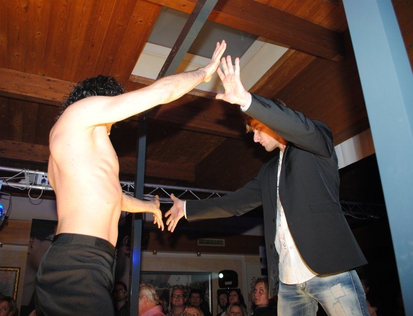 Ein Mann ohne Hemd und ein Mann im Anzug tanzen vor einer Menschenmenge