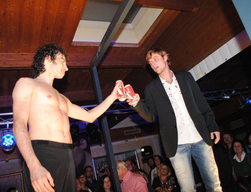 Zwei Männer stoßen vor einer Menschenmenge mit Cola-Dosen an