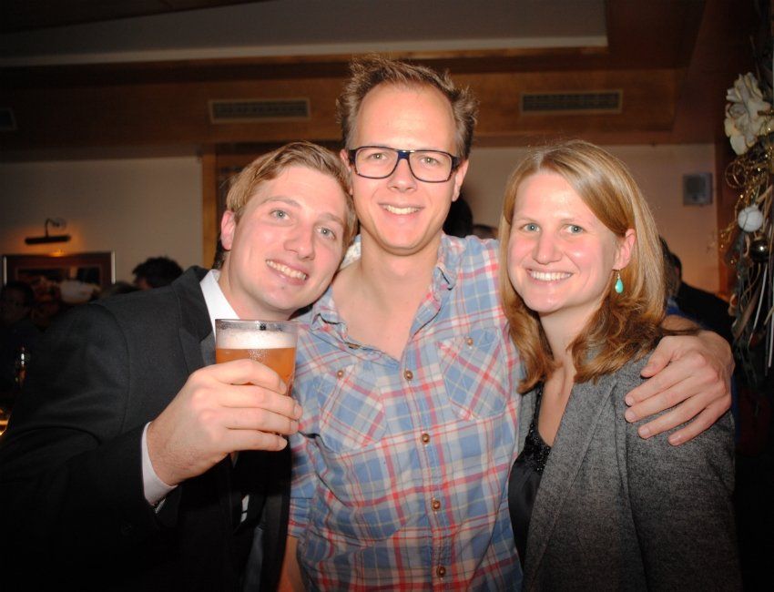 Zwei Männer und eine Frau posieren für ein Foto und ein Mann hält ein Glas Bier