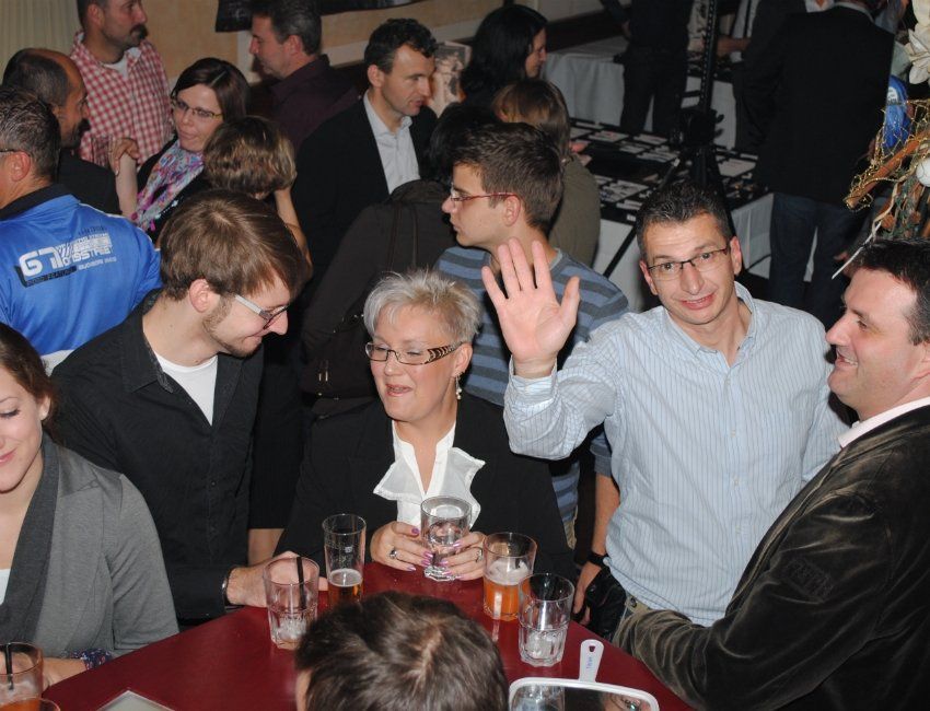 Eine Gruppe von Menschen sitzt um einen Tisch herum, ein Mann trägt ein T-Shirt mit der Aufschrift „g2pro“