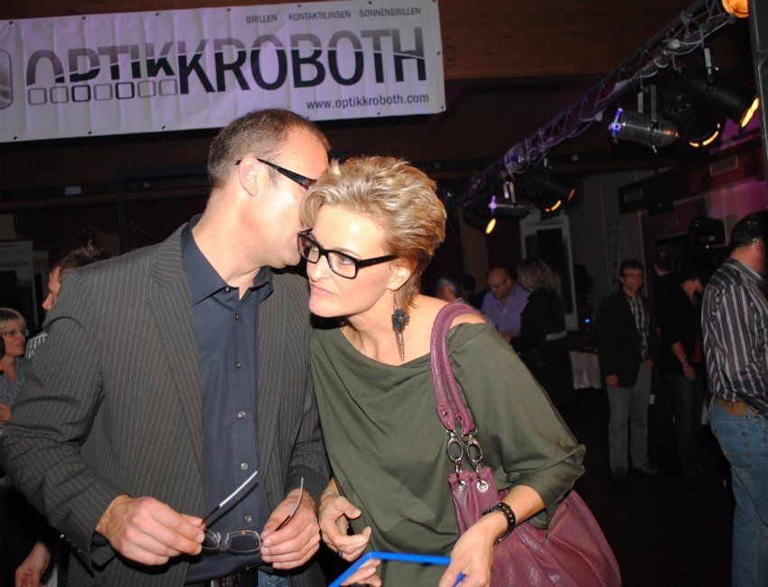 Ein Mann und eine Frau küssen sich vor einem Schild mit der Aufschrift „Optikkroboth“