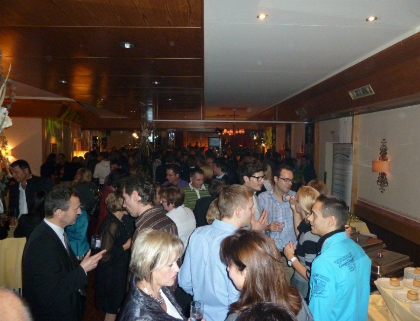 Eine Menschenmenge hat sich in einem Raum versammelt, in dem ein Mann ein blaues Hemd mit der Aufschrift „a“ trägt