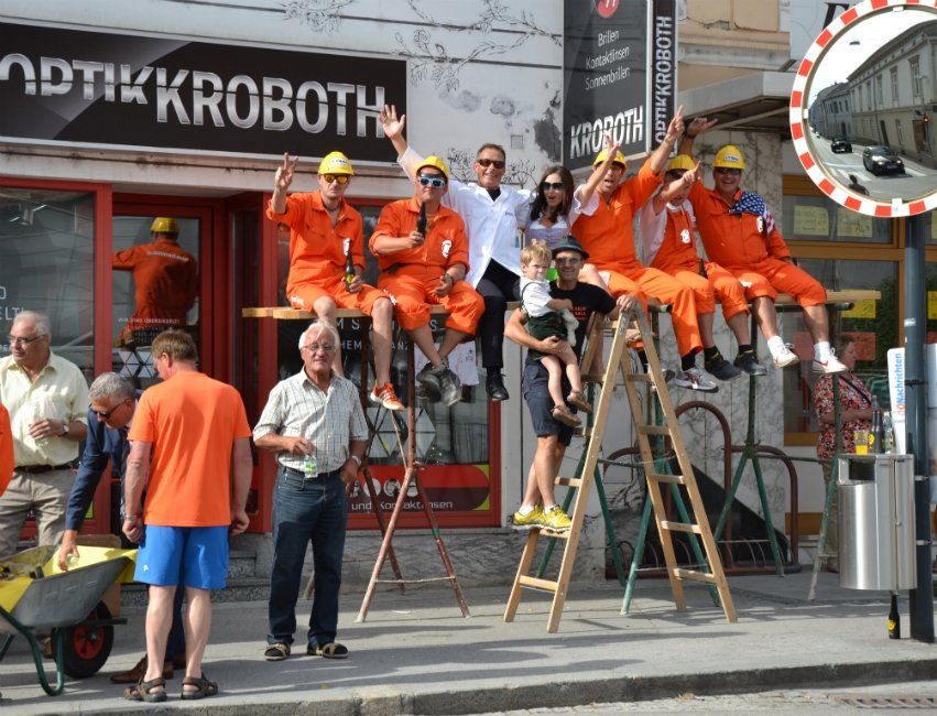 Eine Gruppe von Menschen sitzt auf einer Leiter vor einem Geschäft namens Optikkroboth