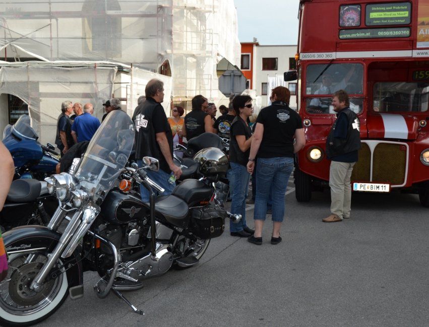 Eine Gruppe von Menschen steht um Motorräder herum vor einem roten Doppeldeckerbus