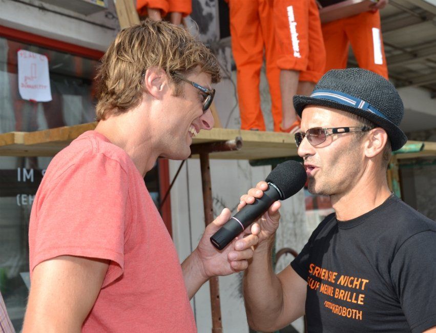 Ein Mann mit Hut und Sonnenbrille spricht in ein Mikrofon