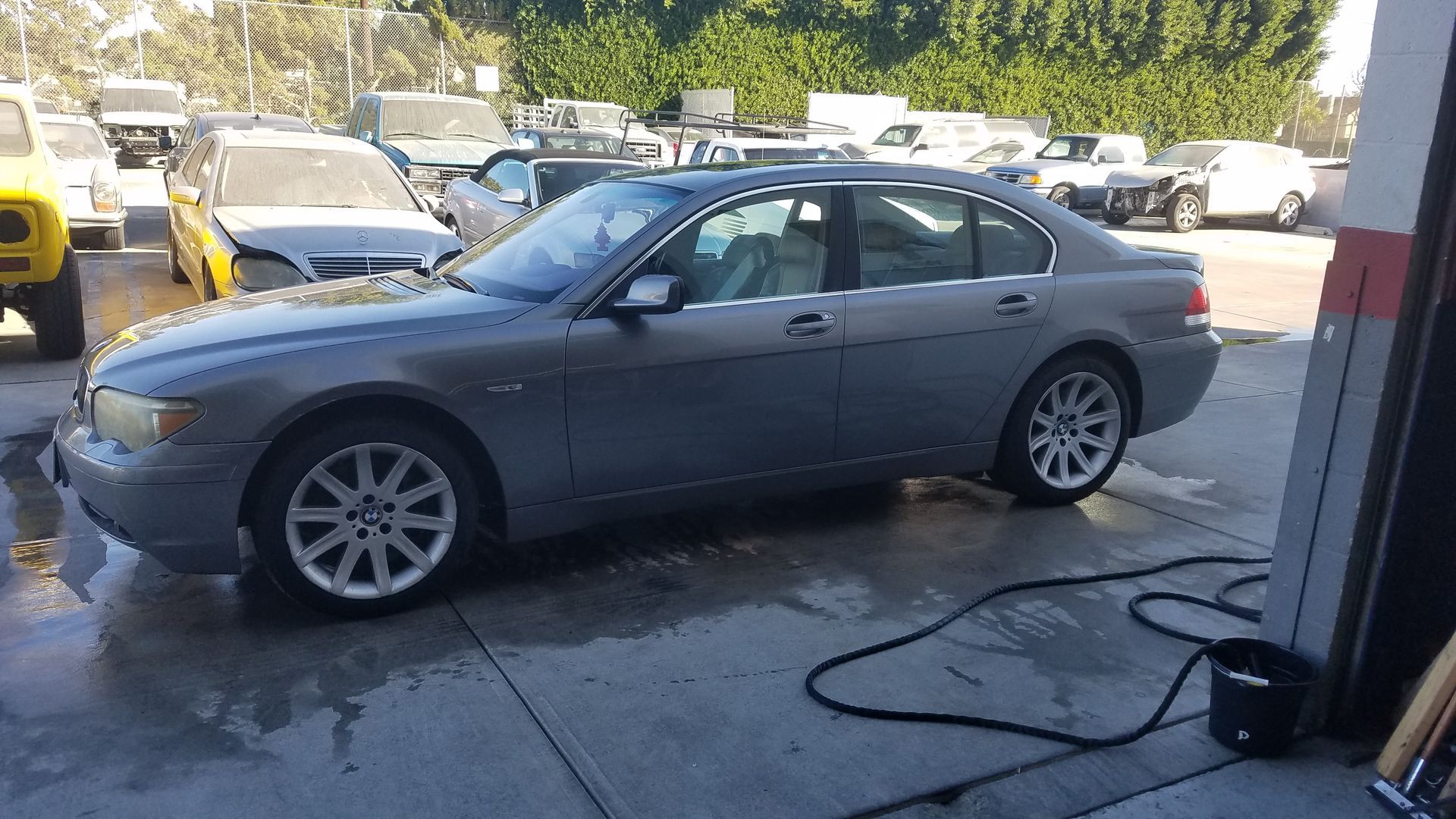 Gray sedan parked in a garage doorway, with other cars and a hose on the concrete outside.