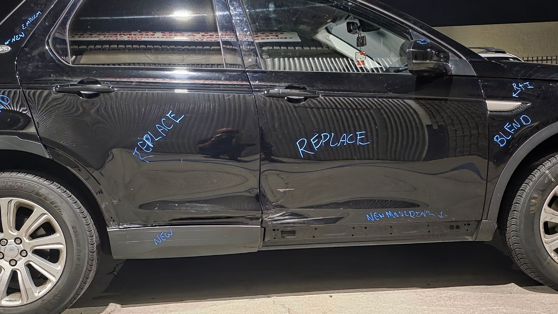 Black sedan with dents and scuffs along the side, parked outdoors.