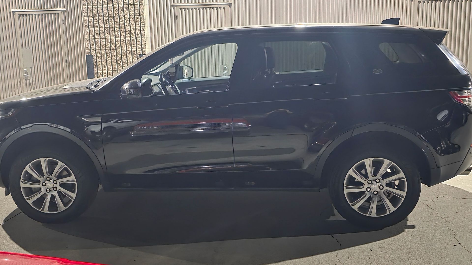 Black SUV parked in profile on a street beside a wooden fence.