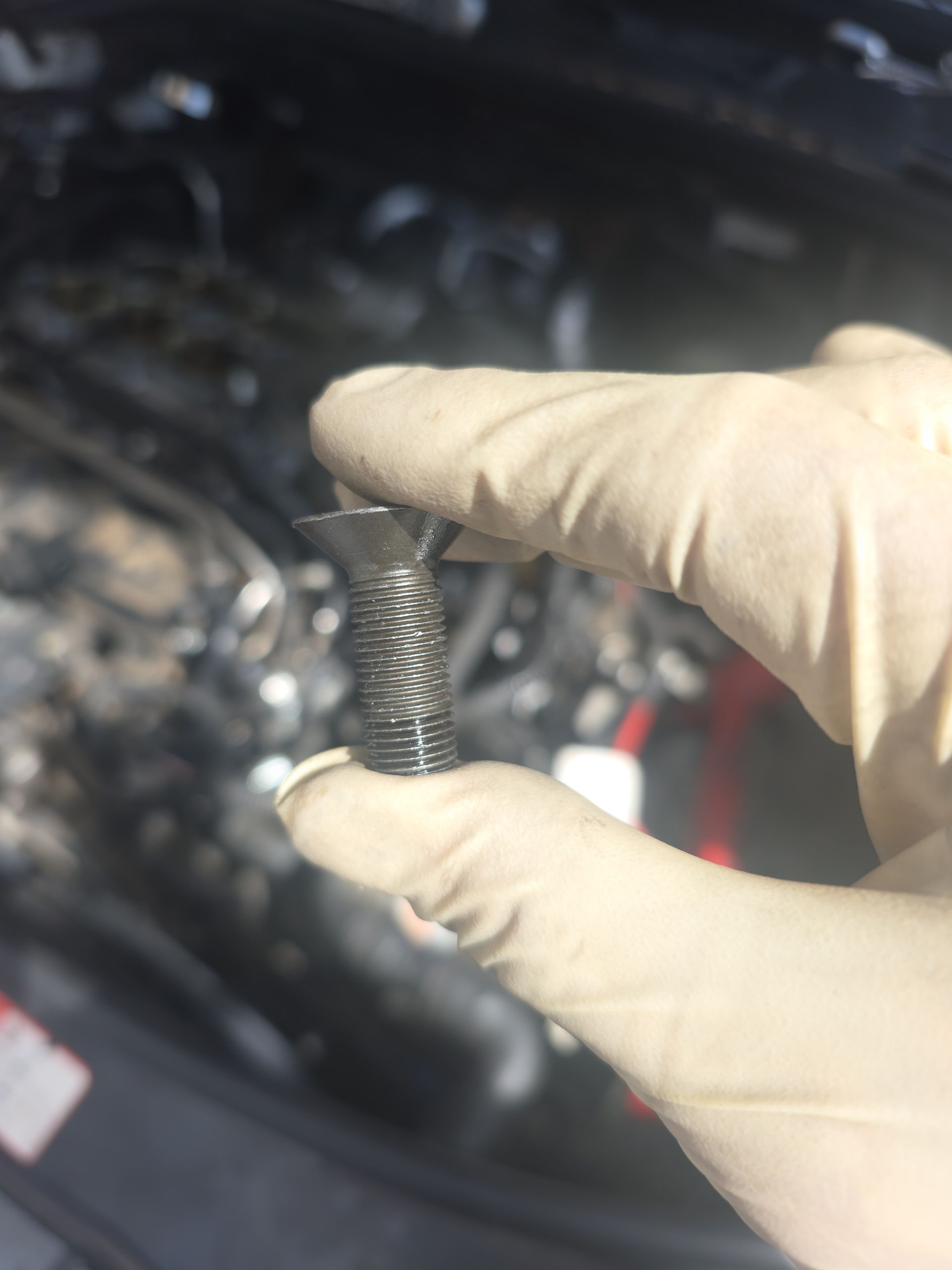Gloved hand holding a small metal spring over an engine bay