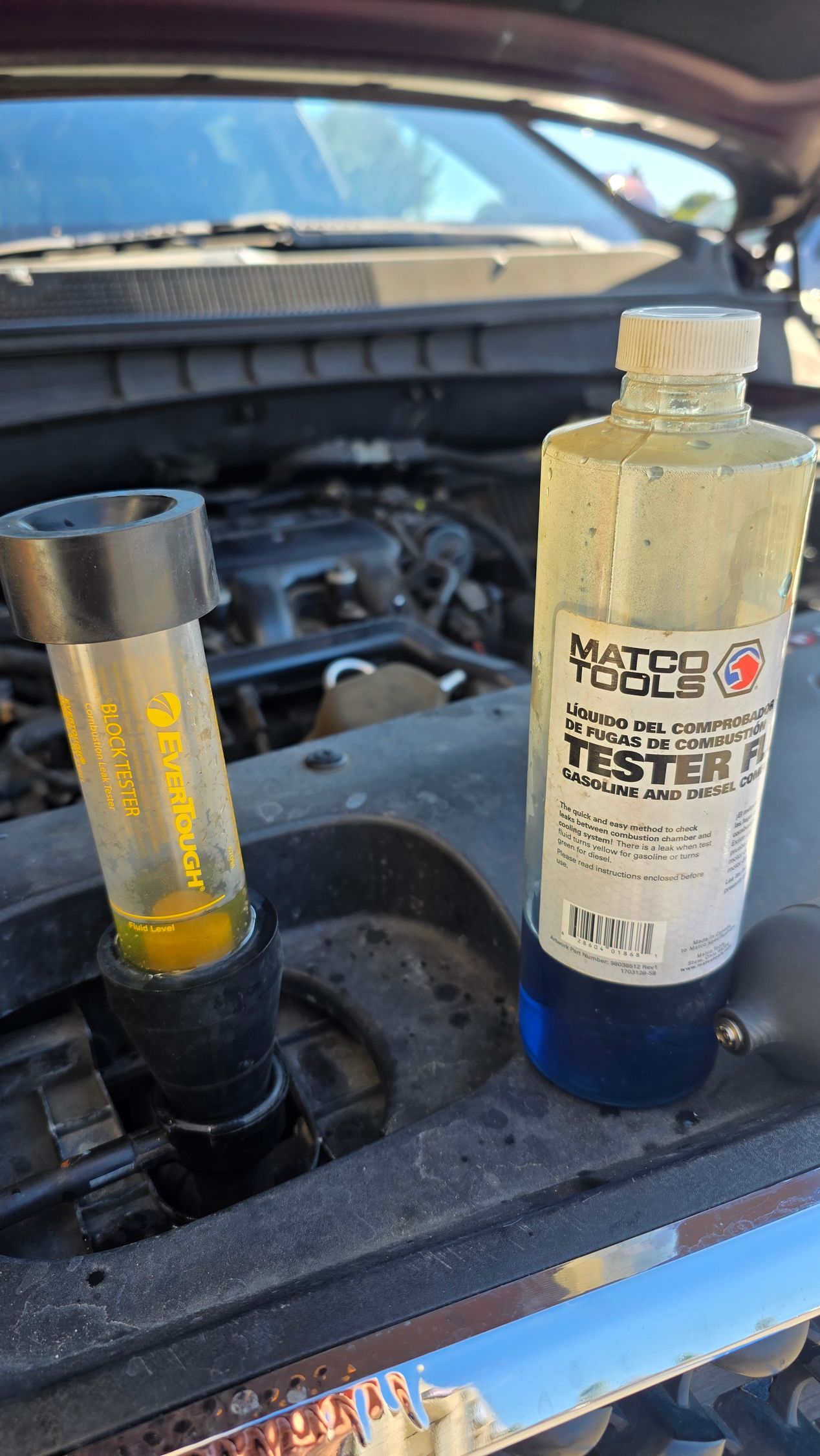 Two engine-oil dipstick tubes in a car’s engine bay, one with yellow fluid and one labeled bottle beside it.