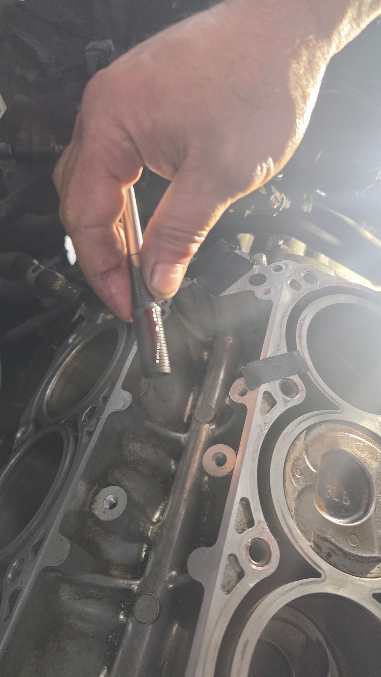 Hand holding a tool inside an open engine bay beside exposed metal parts and gaskets