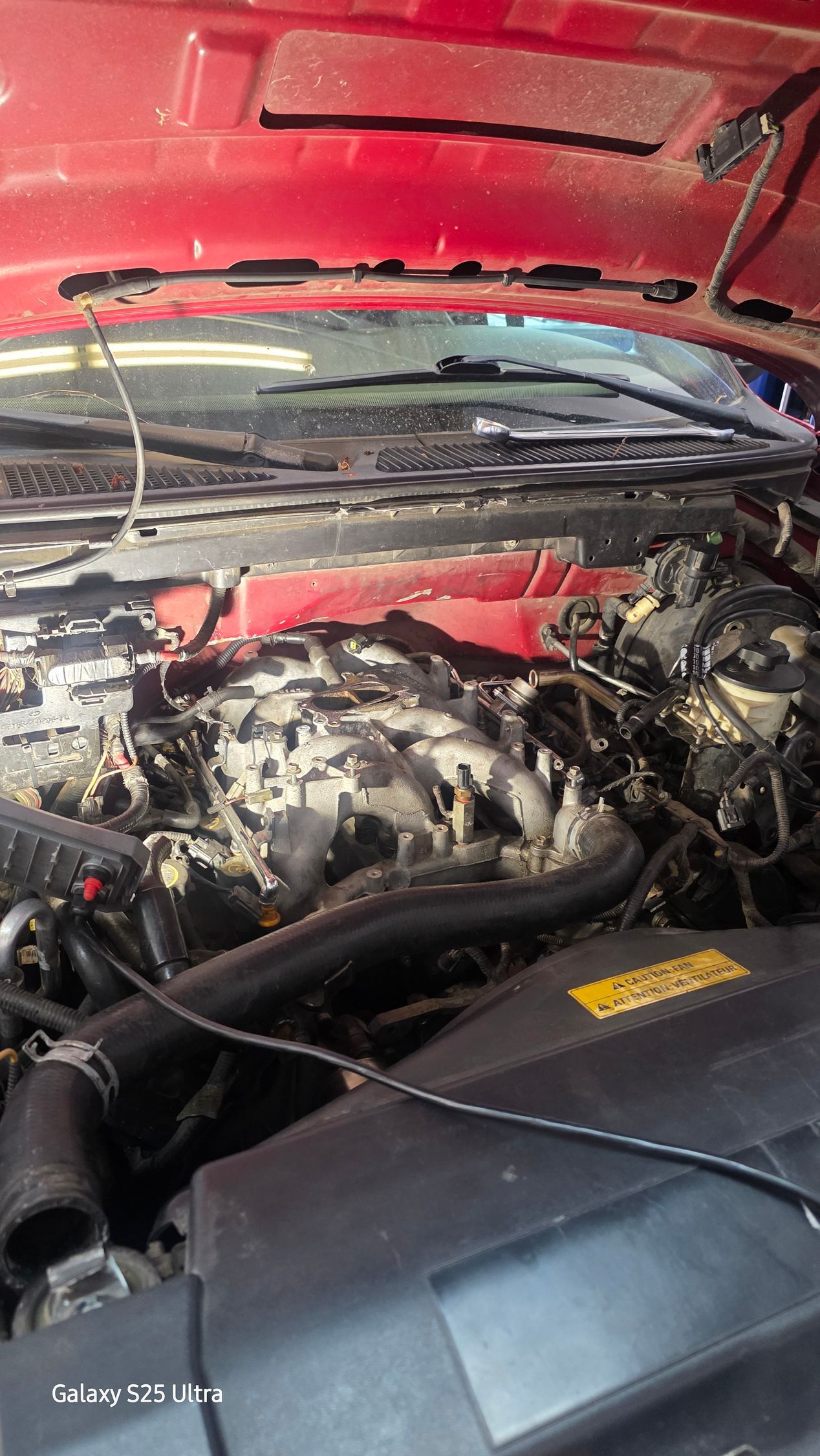 Open car hood with red underside, showing engine bay and air intake components.