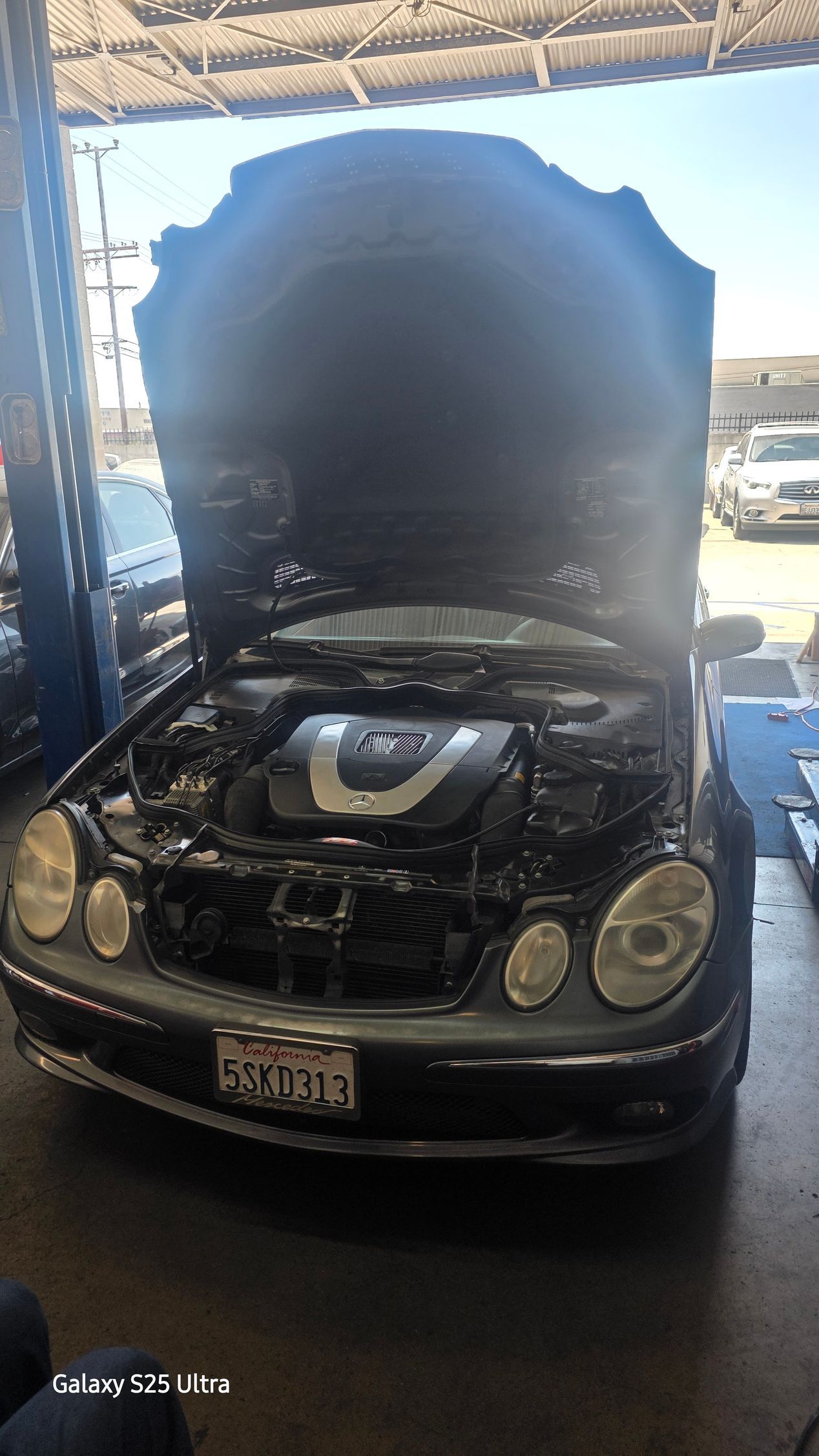 Auto repair shop entrance with cars and a lift inside, under a sign above the garage bay