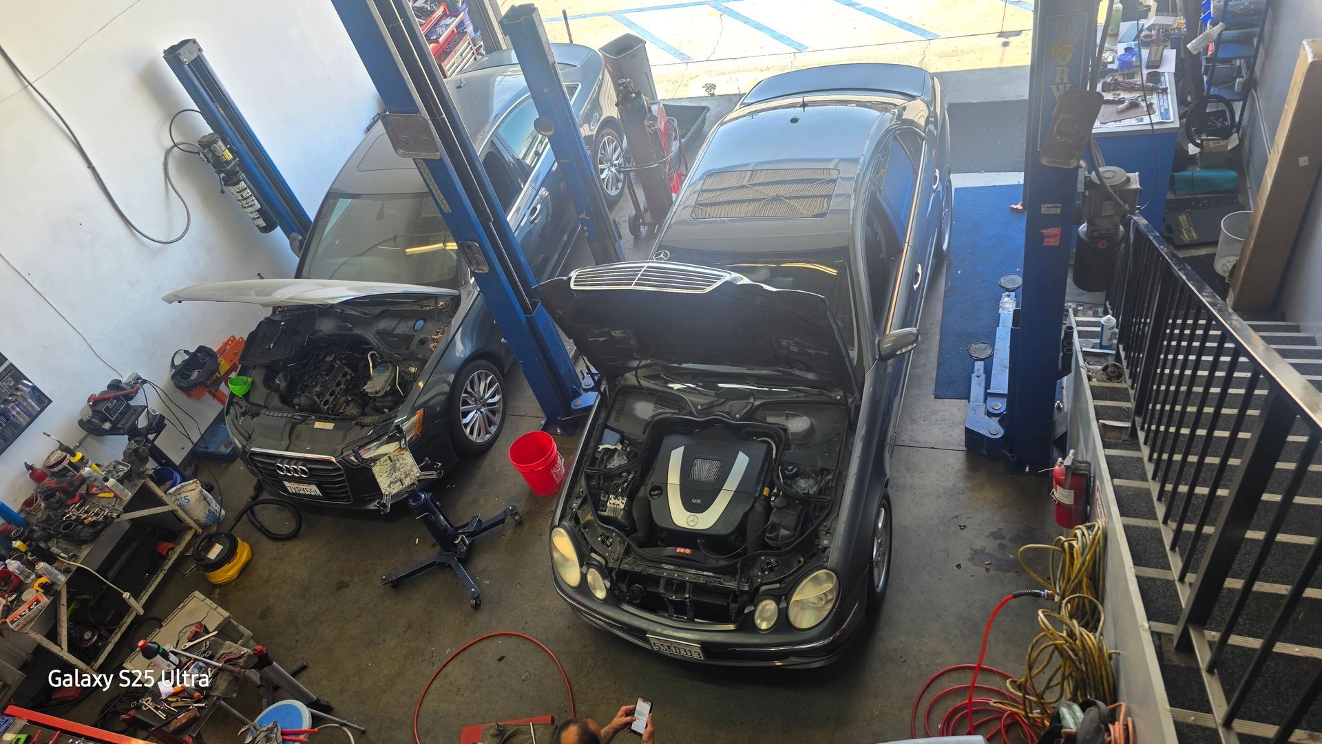 Black car in a mechanic’s garage on a lift, surrounded by tools and equipment.
