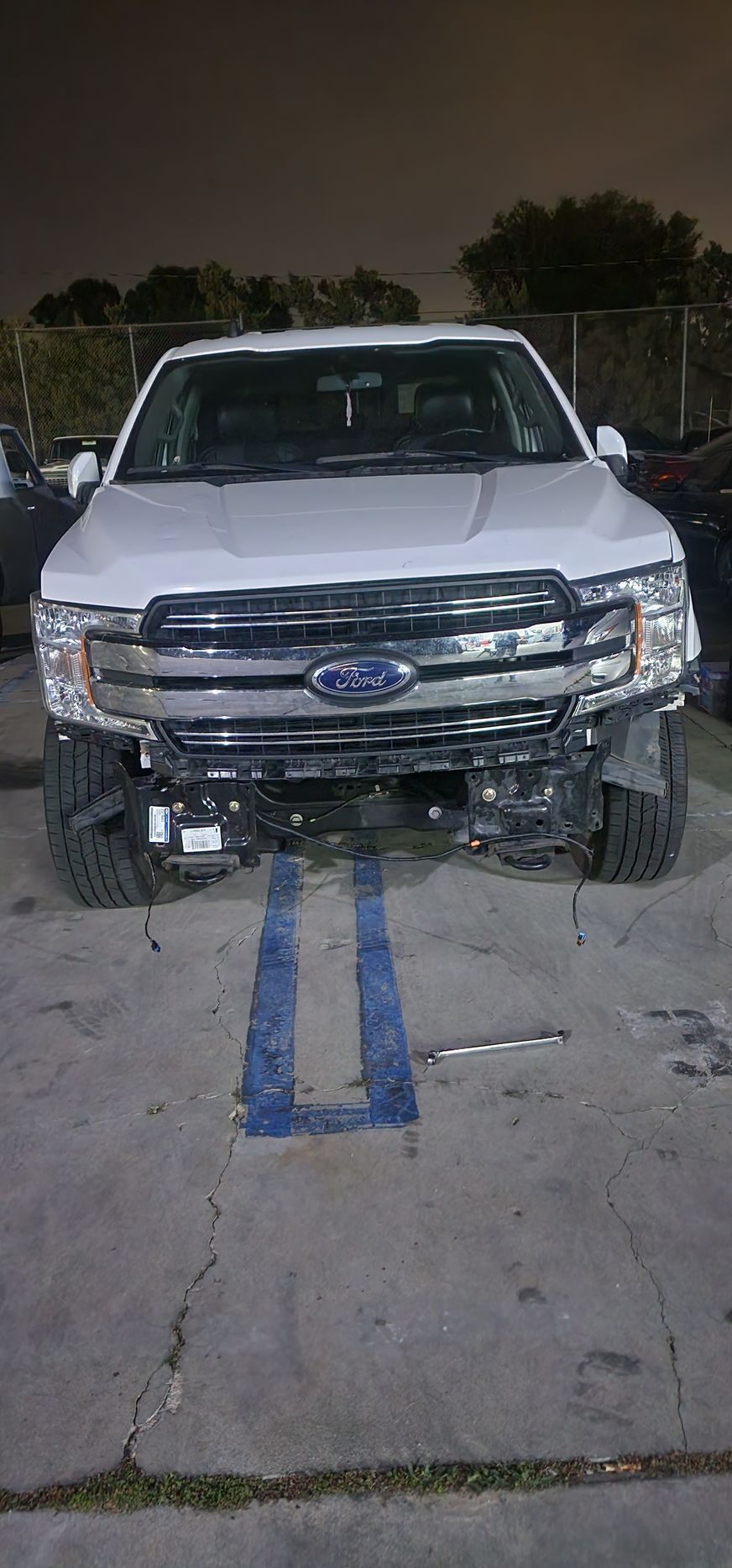 White pickup truck with front-end damage parked on a driveway at night