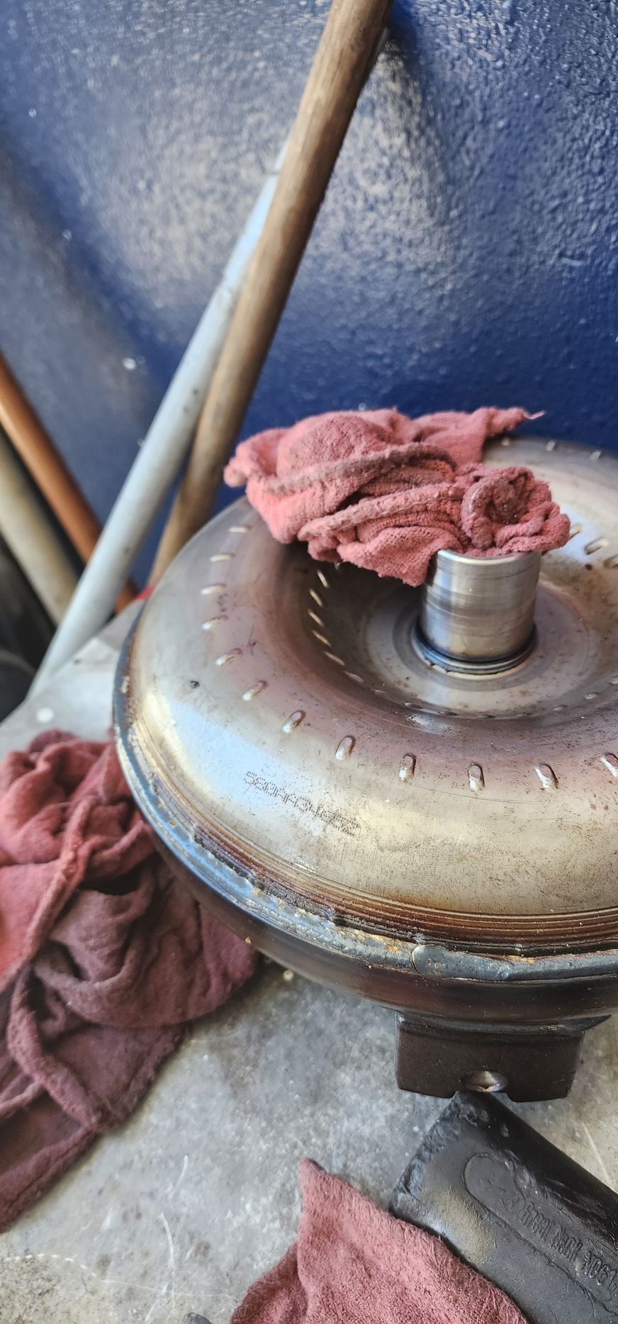 Rusty metal pot lid with a cloth rag draped over it, on a dusty blue surface with pipes nearby