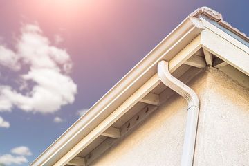 The roof of a house with a white gutter and a blue sky in the background.