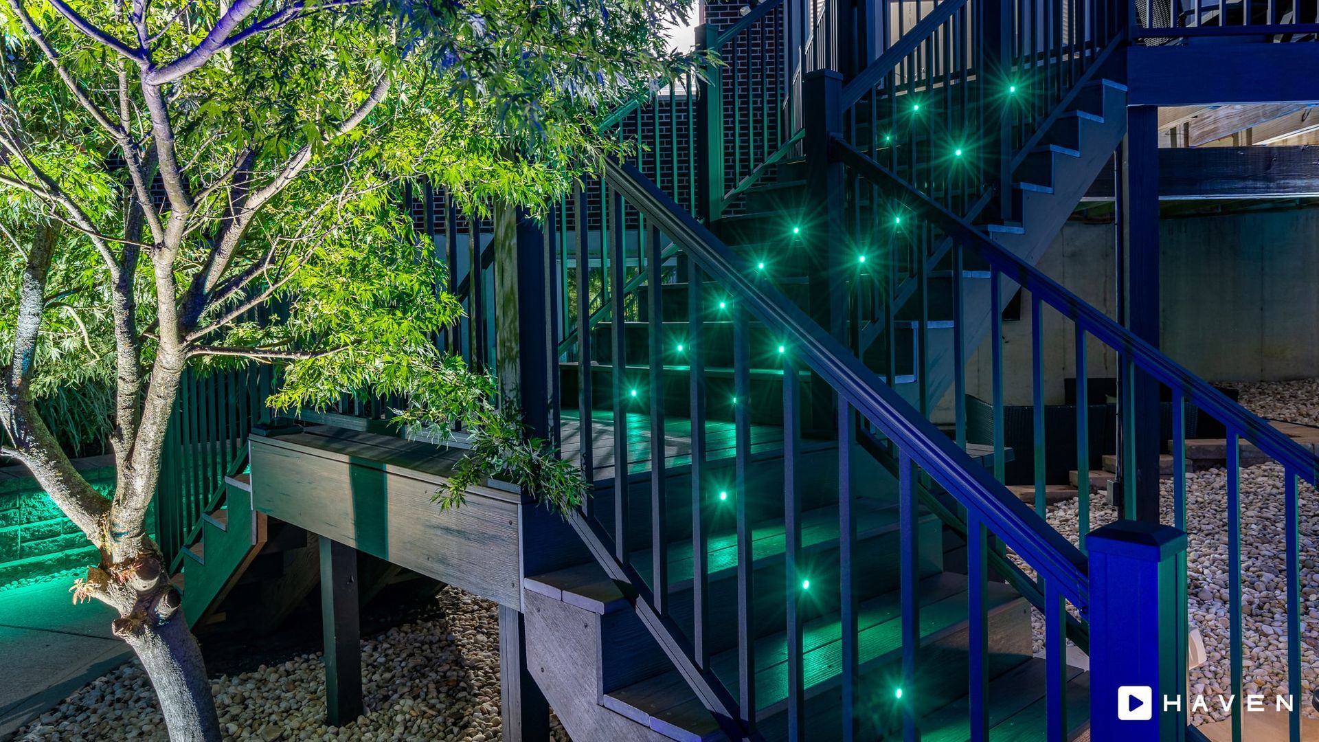 A set of stairs with green lights on them and a tree in the background.