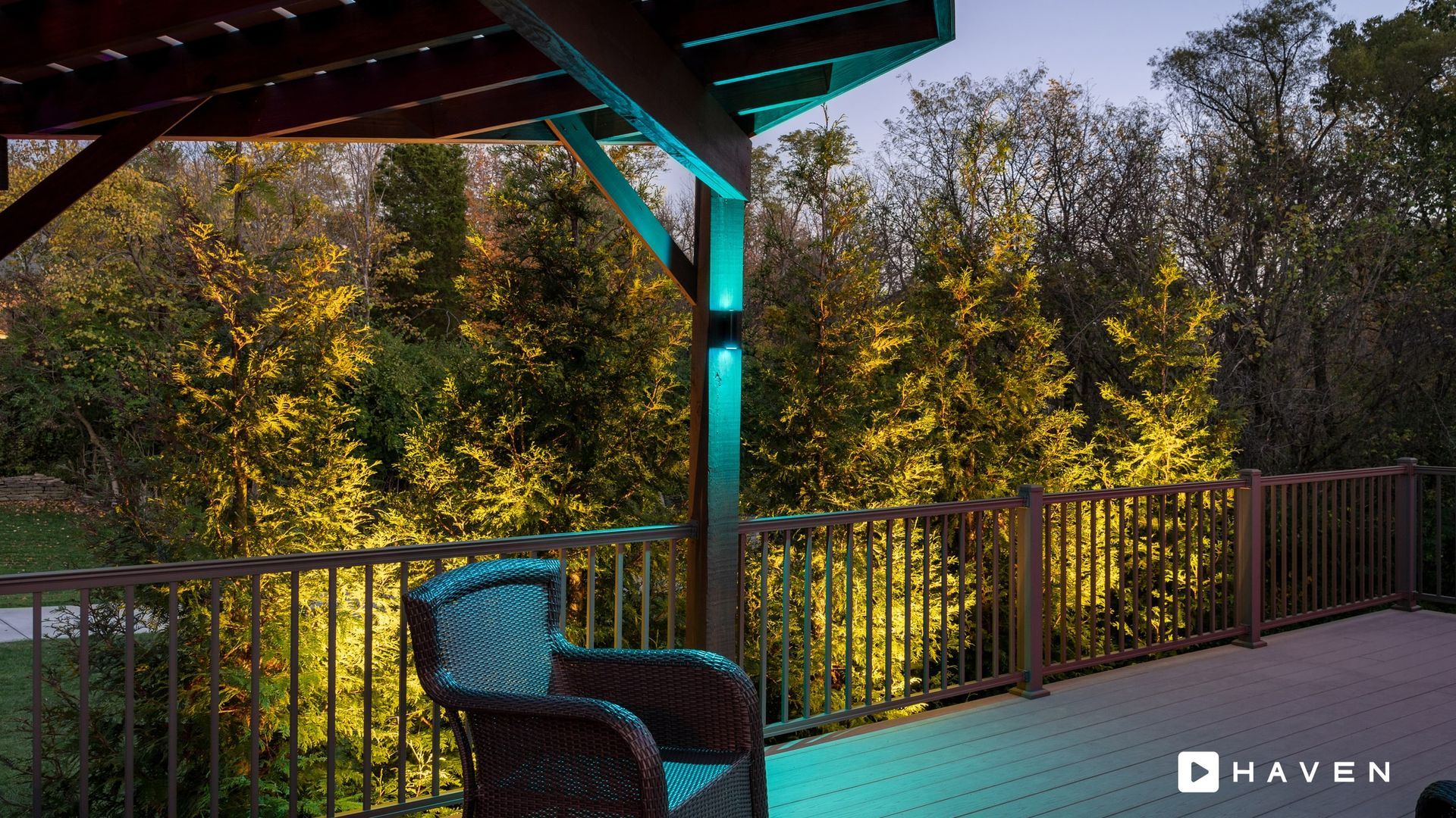 A deck with a chair and a fence with trees in the background