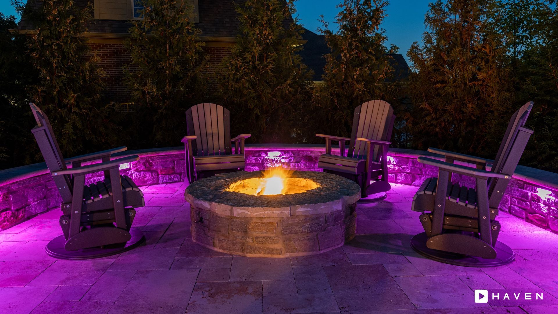 A fire pit surrounded by chairs and purple lights on a patio.