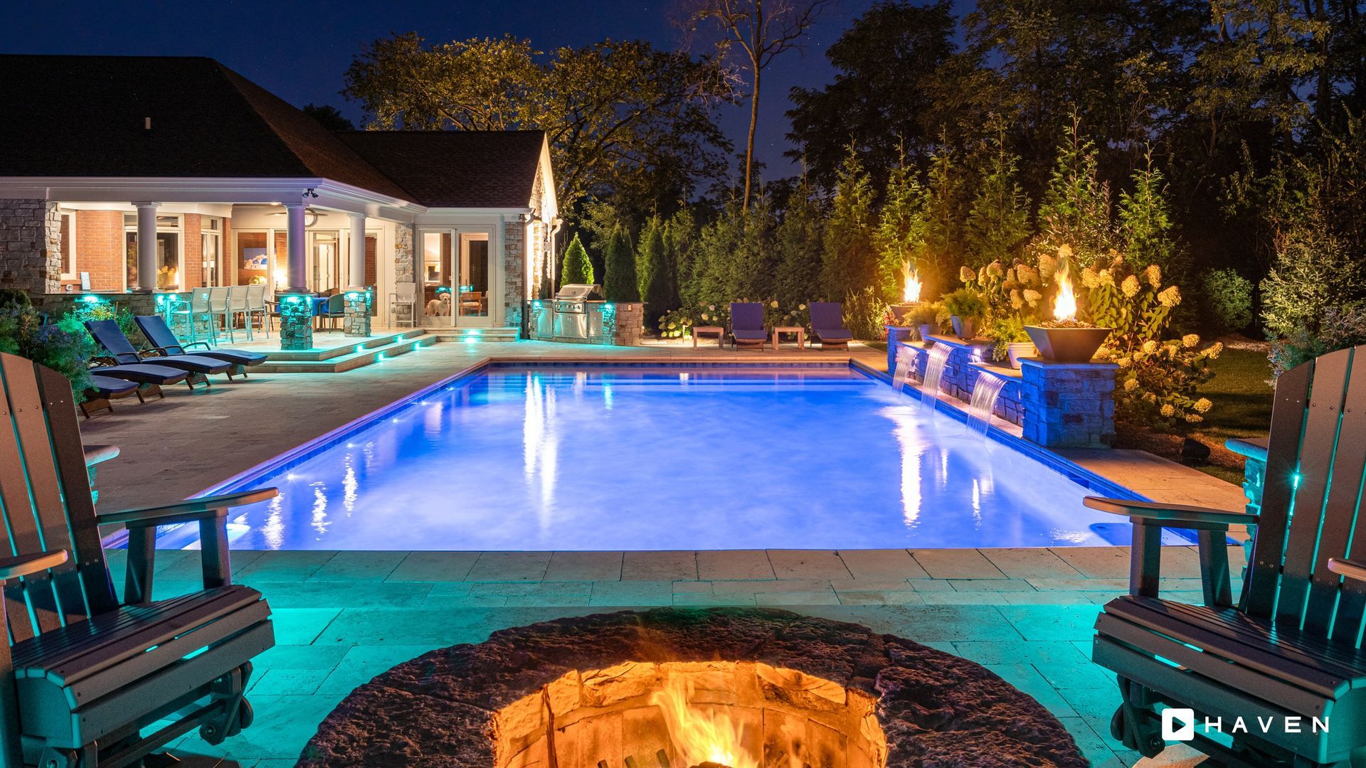 A large swimming pool with a fire pit in the middle of it at night.