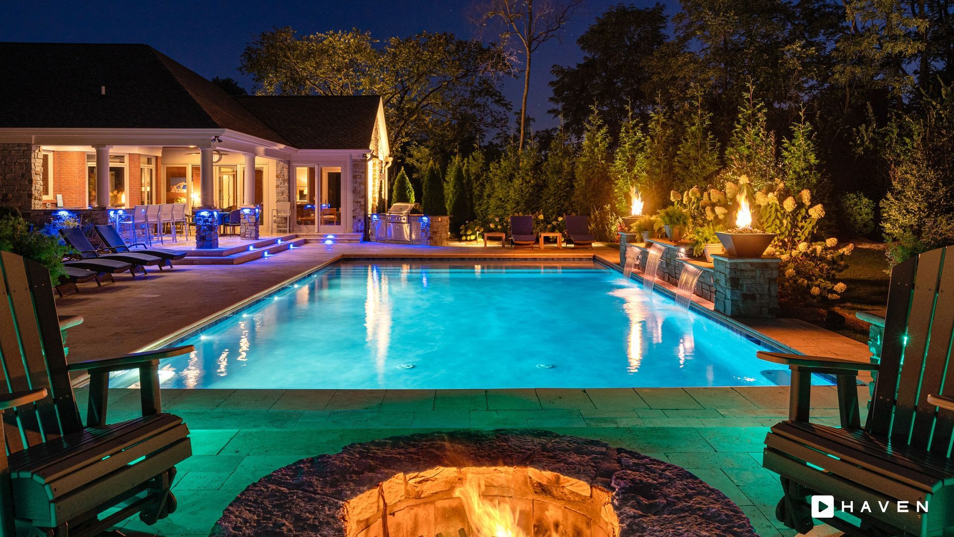 A fire pit in front of a large swimming pool at night