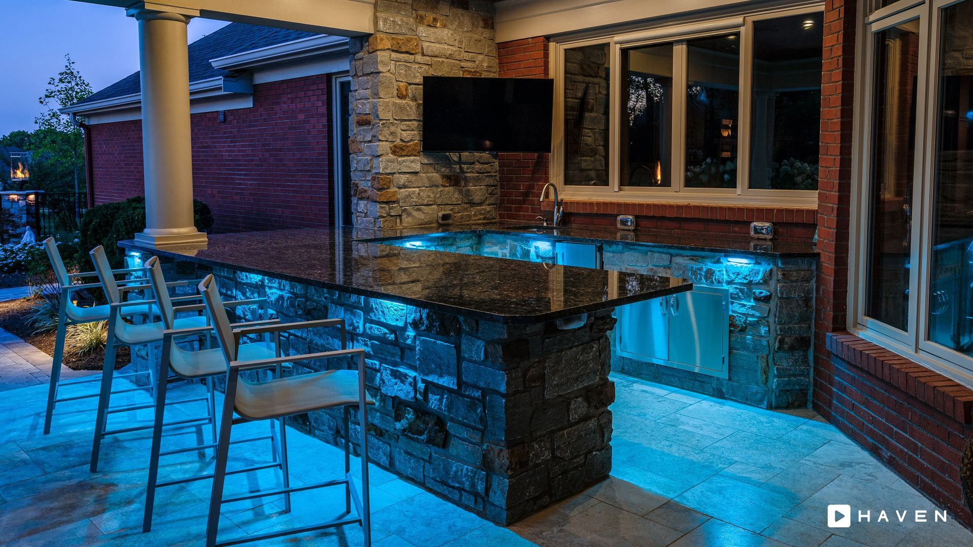 A kitchen with a bar and stools and a television on the wall.