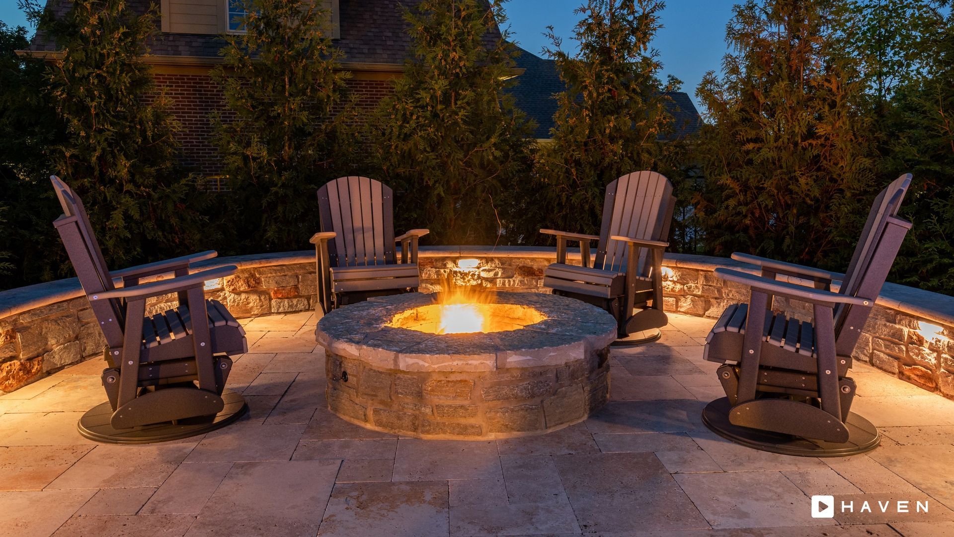 A fire pit surrounded by chairs on a patio at night.