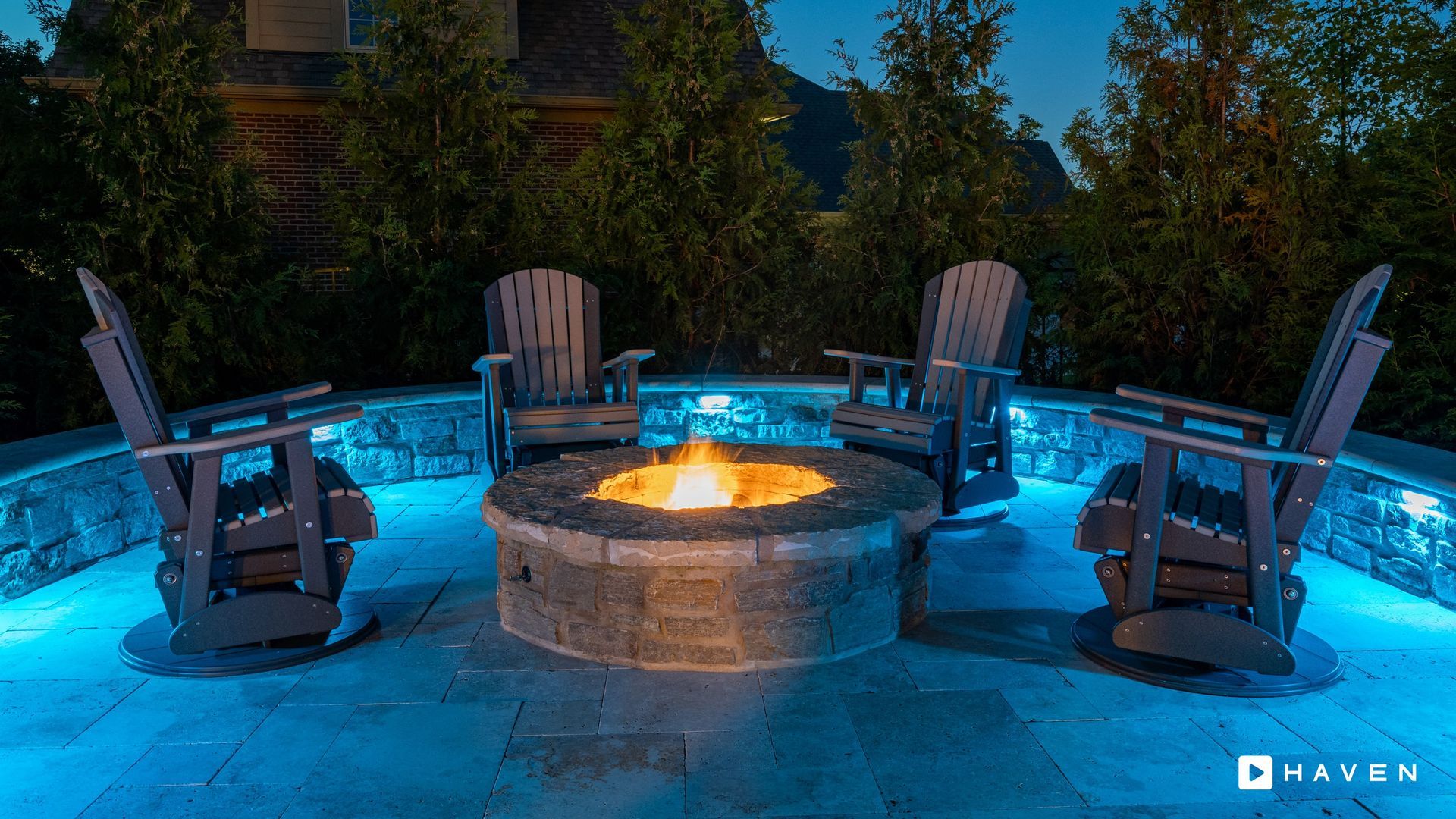 A fire pit with chairs around it is lit up at night.