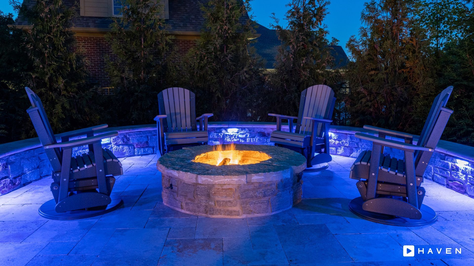 A fire pit with chairs around it is lit up at night.