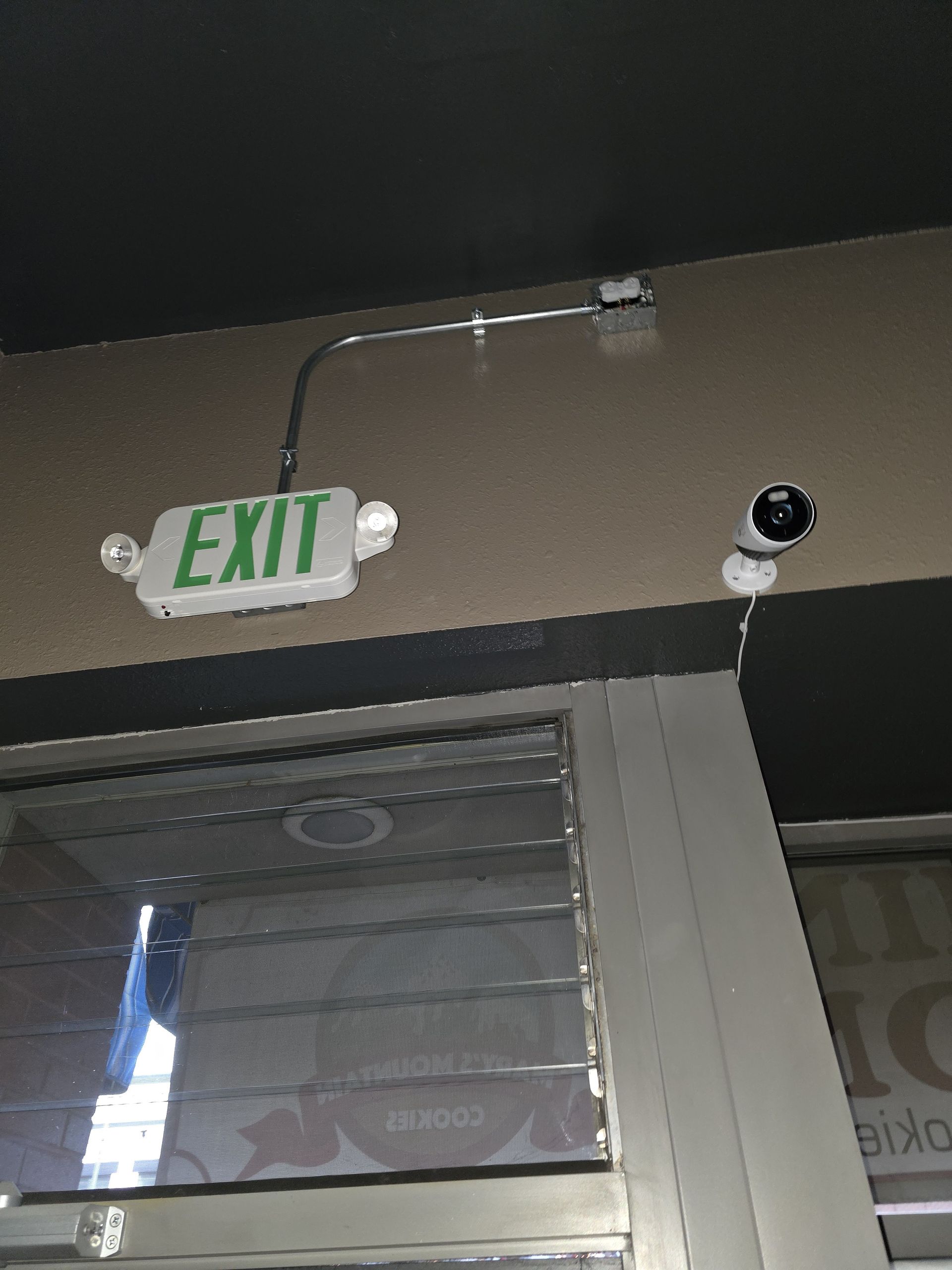 Exit sign and security camera above a window.