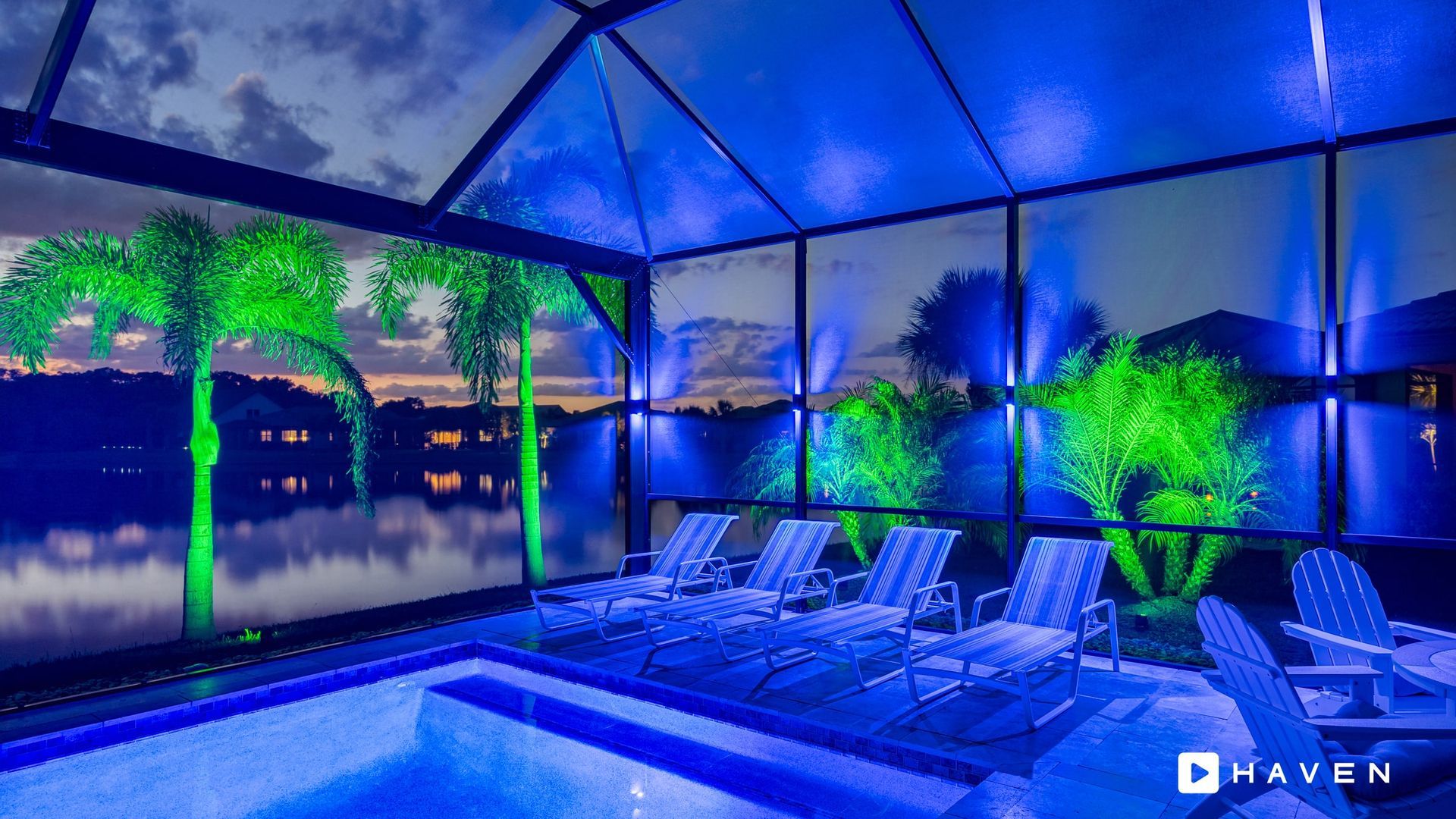 A swimming pool with chairs and a view of a lake at night.