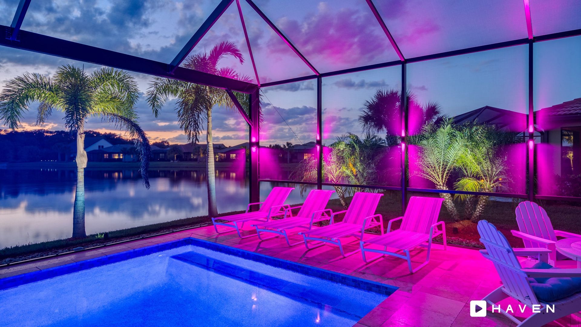 A swimming pool with purple chairs and a view of a lake at night.