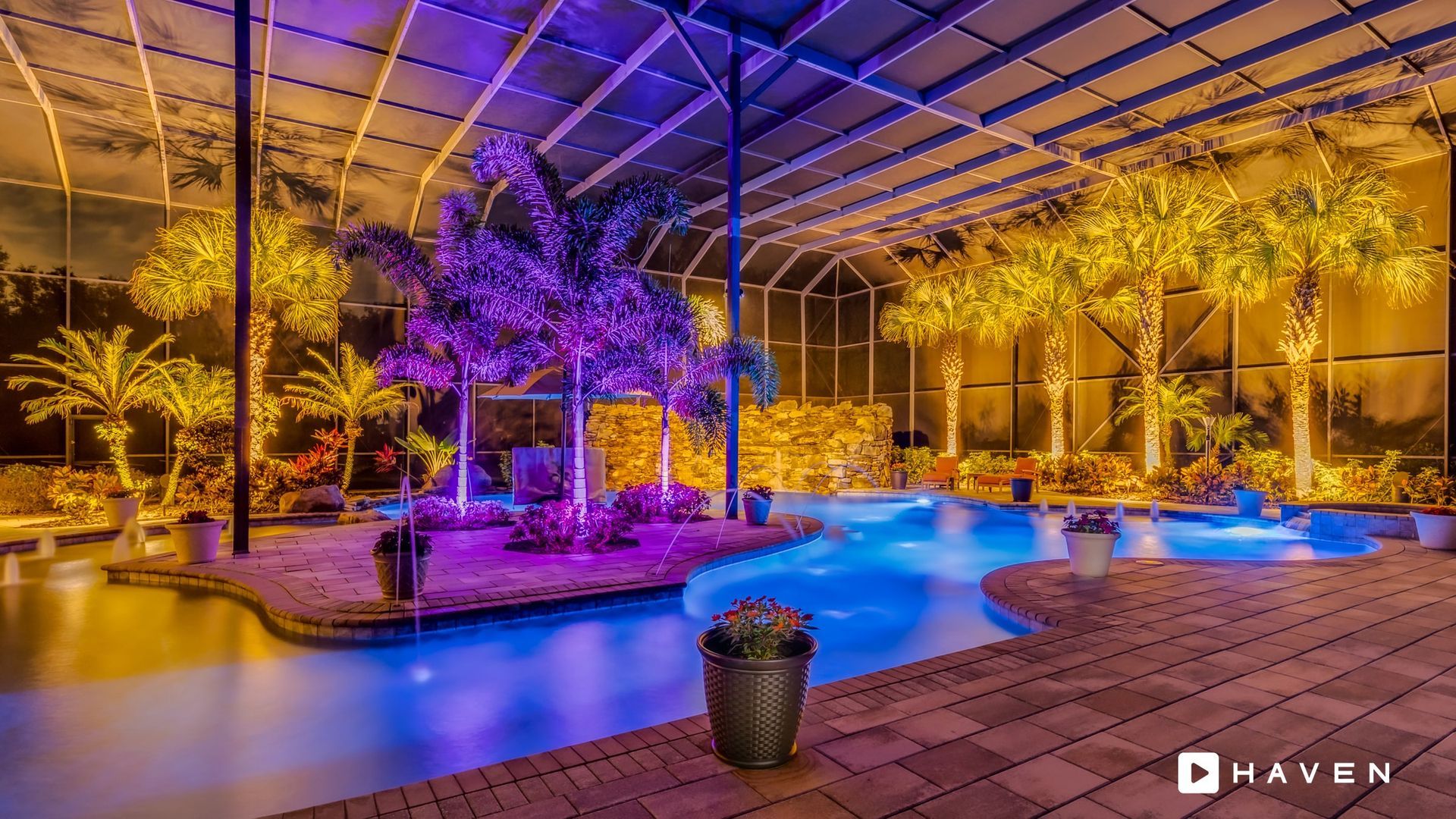 A large swimming pool is lit up at night with purple and yellow lights.