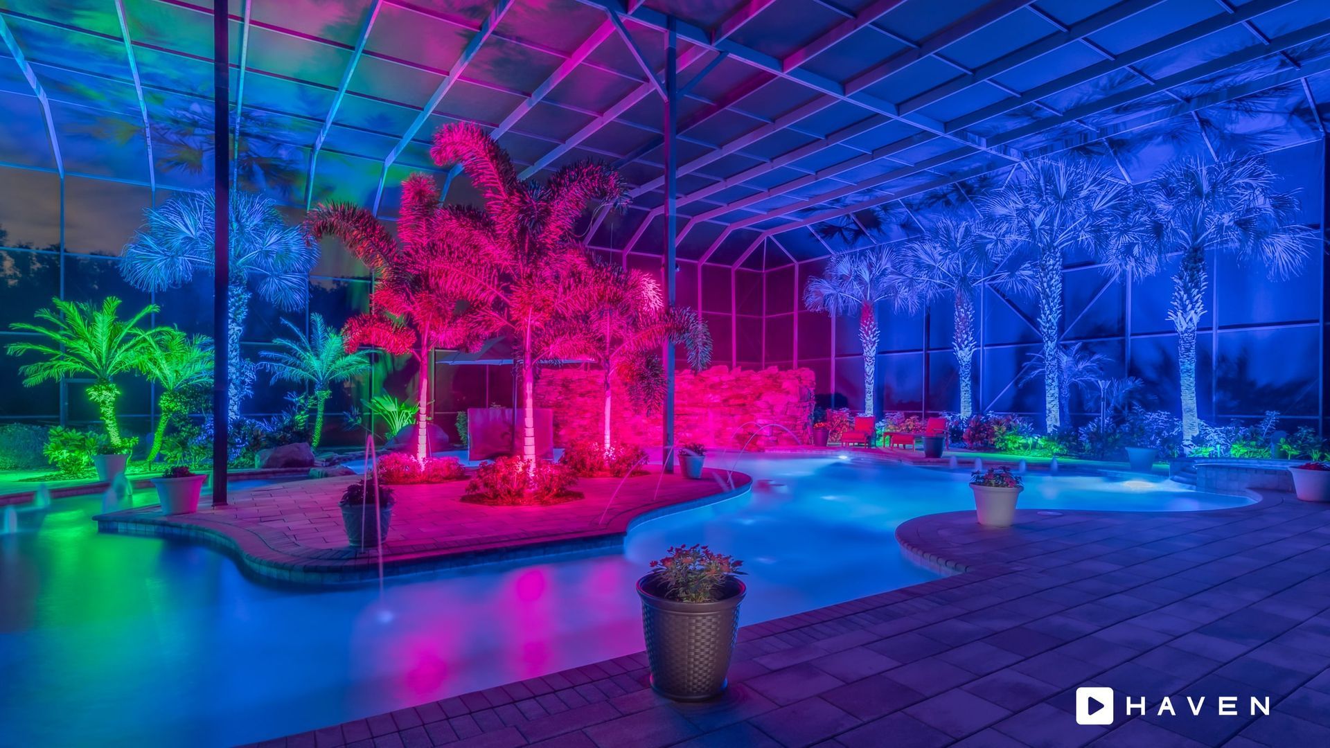 A swimming pool is lit up with neon lights and palm trees.