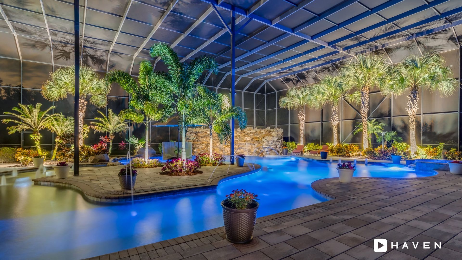 A large swimming pool is lit up at night surrounded by palm trees.
