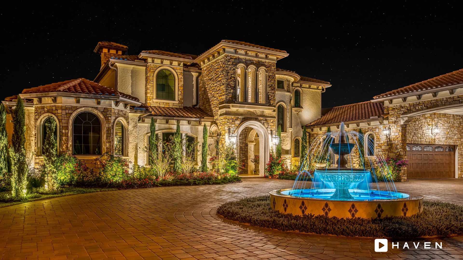 A large house with a fountain in front of it at night.