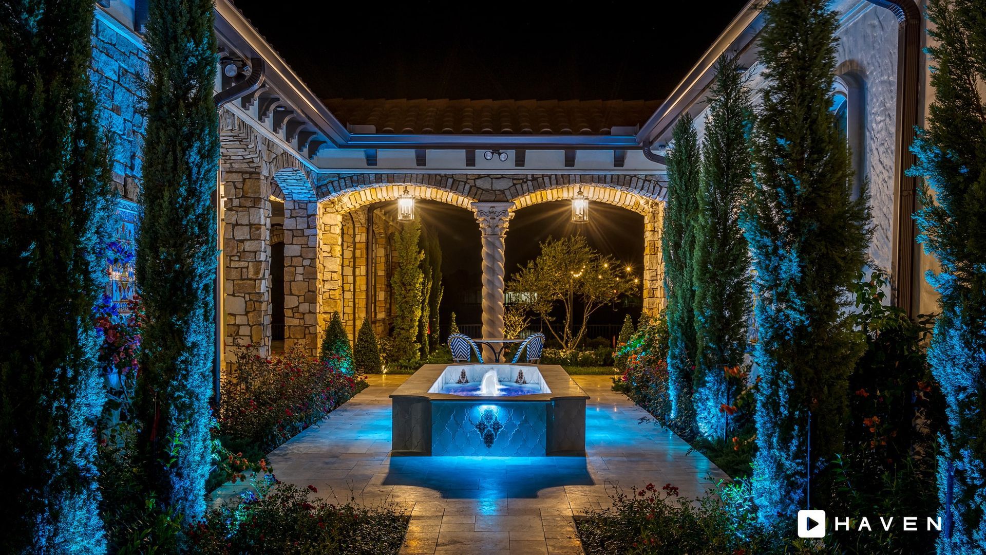 A large swimming pool is surrounded by trees and a building at night.