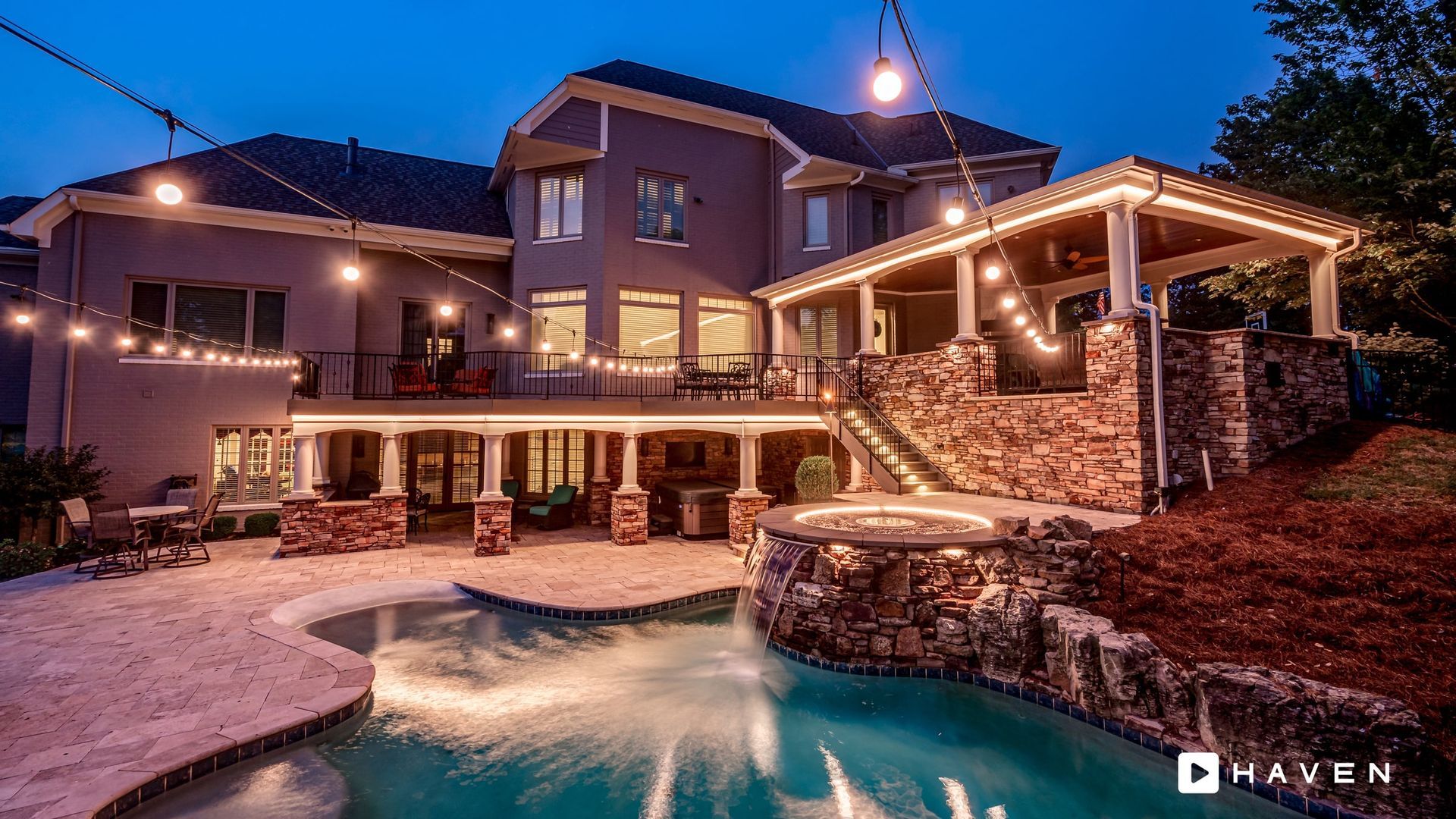 A large house with a swimming pool in front of it at night.