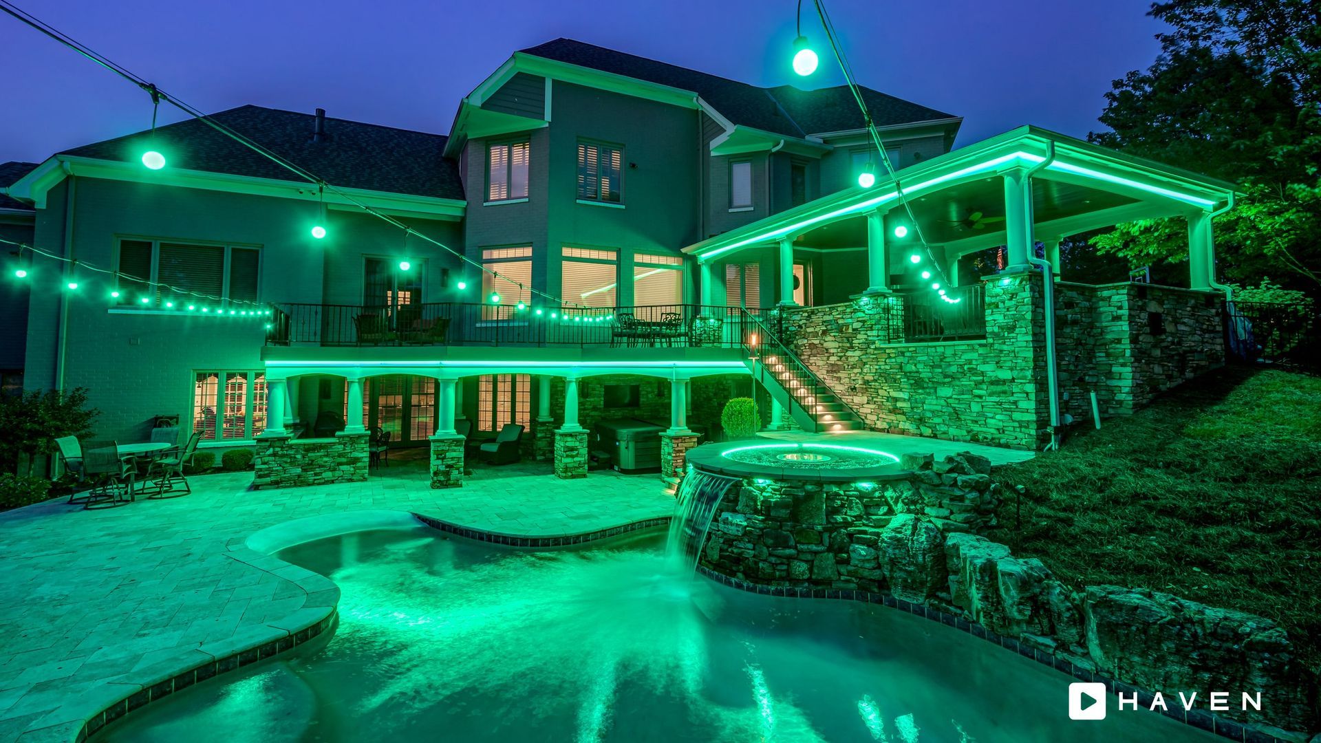 A large house with a swimming pool is lit up with green lights.