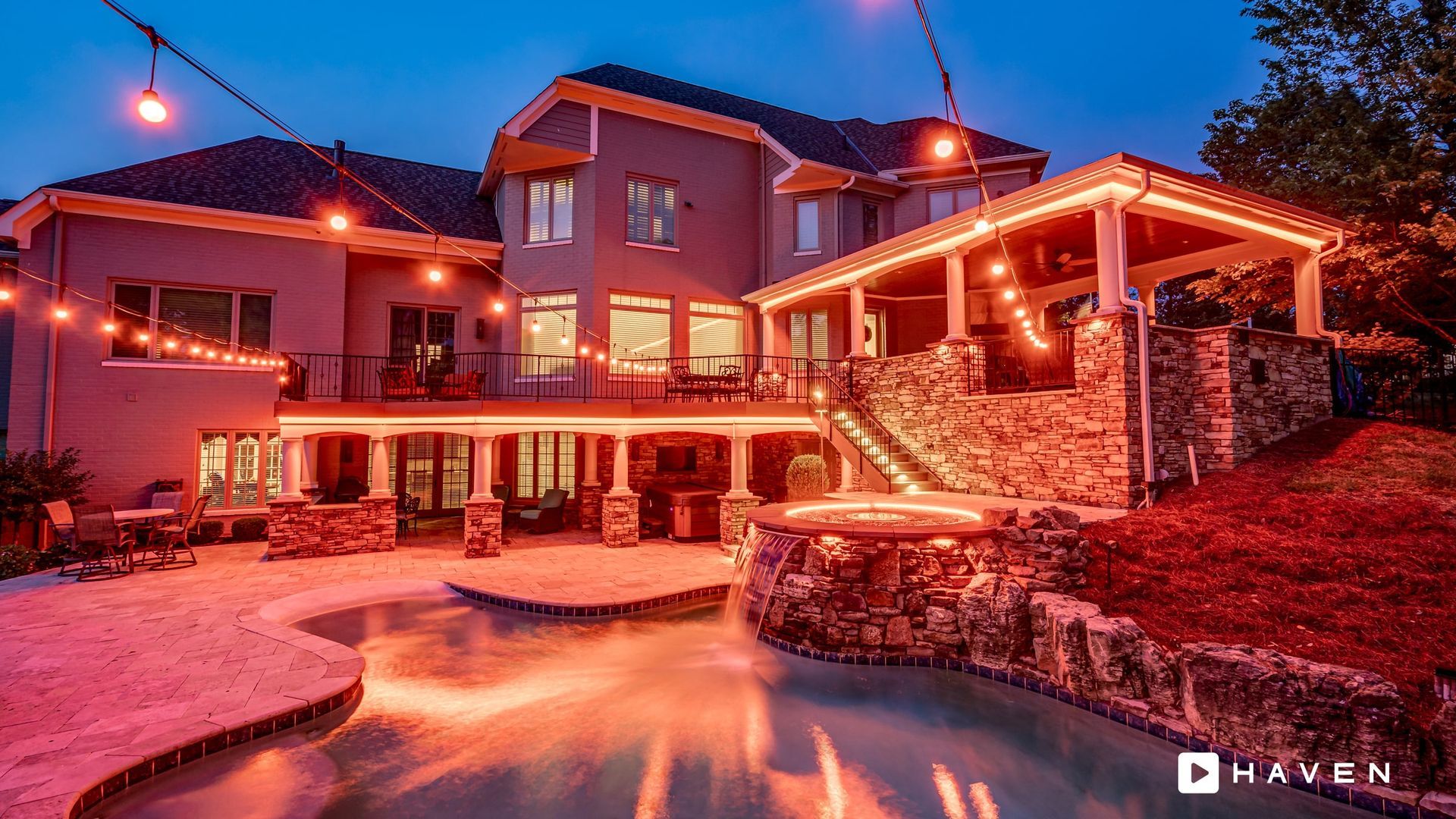A large house with a swimming pool in front of it at night.